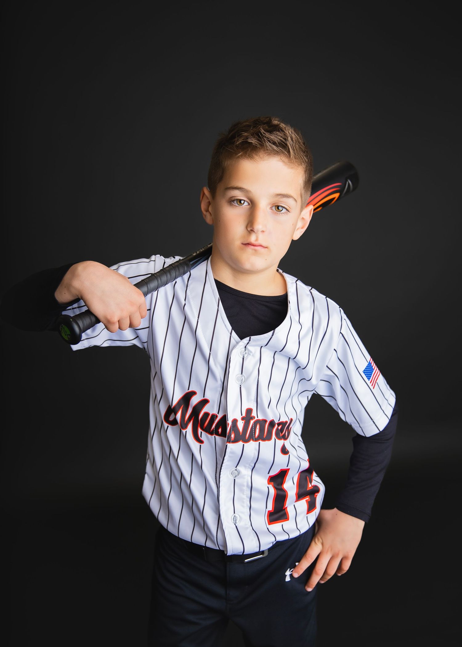 Youth baseball player in Mustangs pinstripe jersey number 15 poses confidently with bat resting on shoulders.