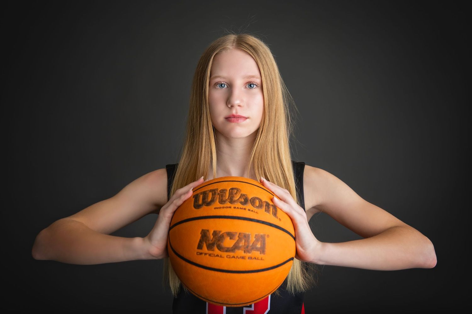 Blonde teen girl in black Attack jersey holding Wilson NCAA basketball.