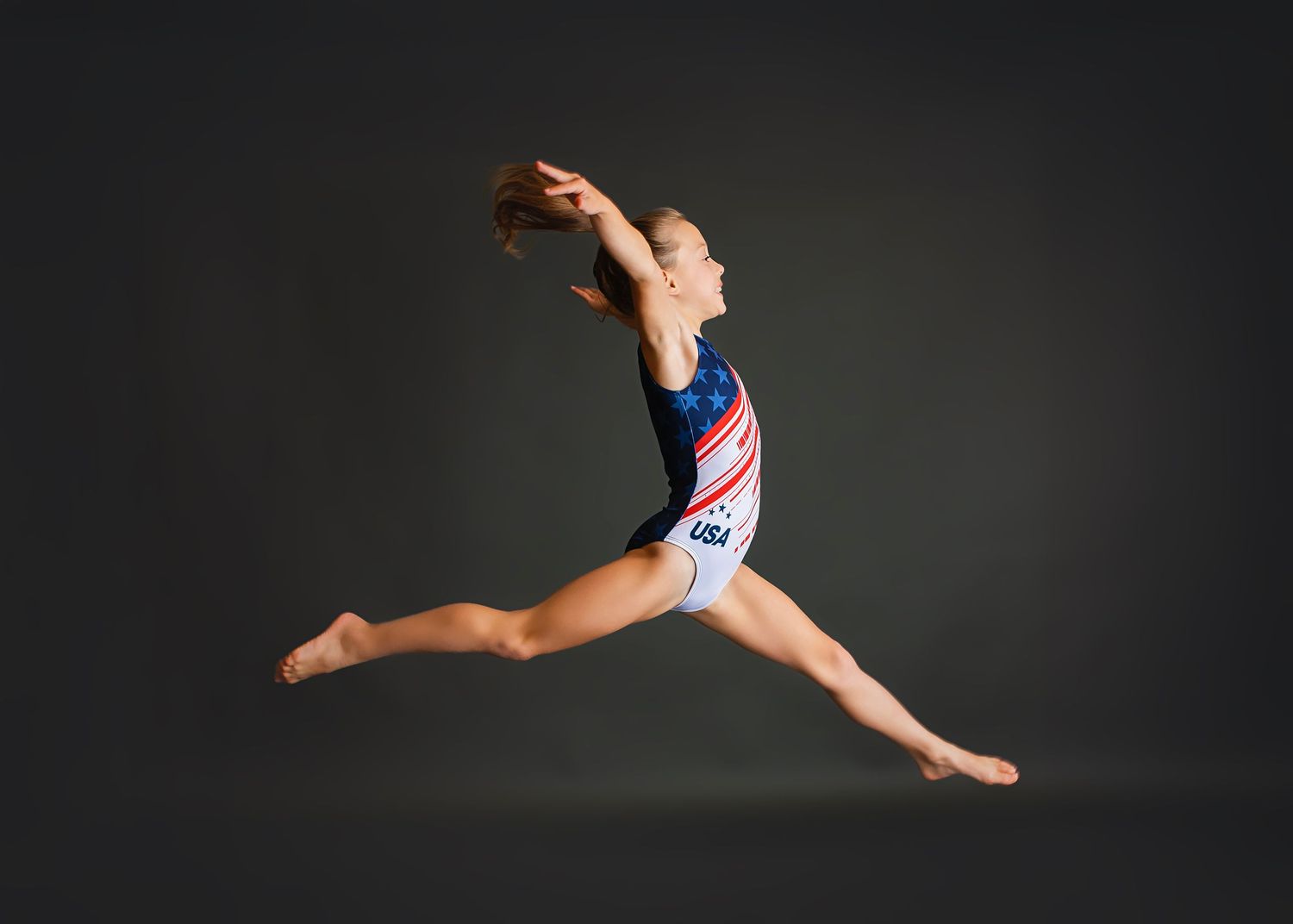 Young gymnast in USA leotard performs a spectacular mid-air split leap.