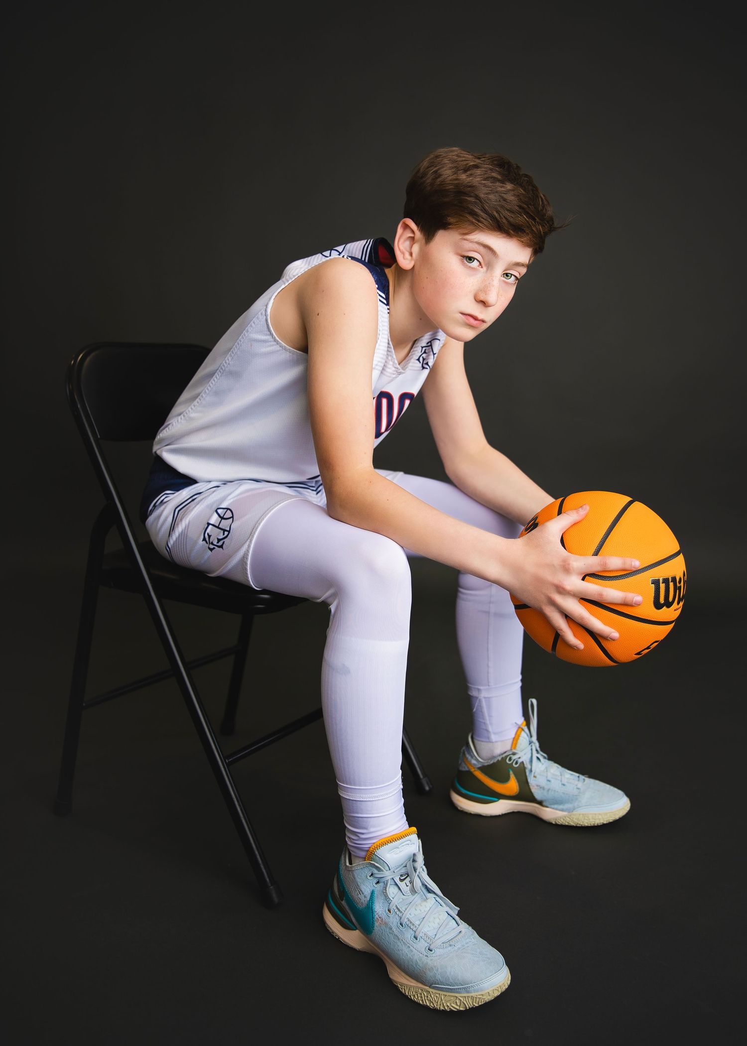Young boy in white basketball uniform sitting on a chair holding a Wilson basketball.