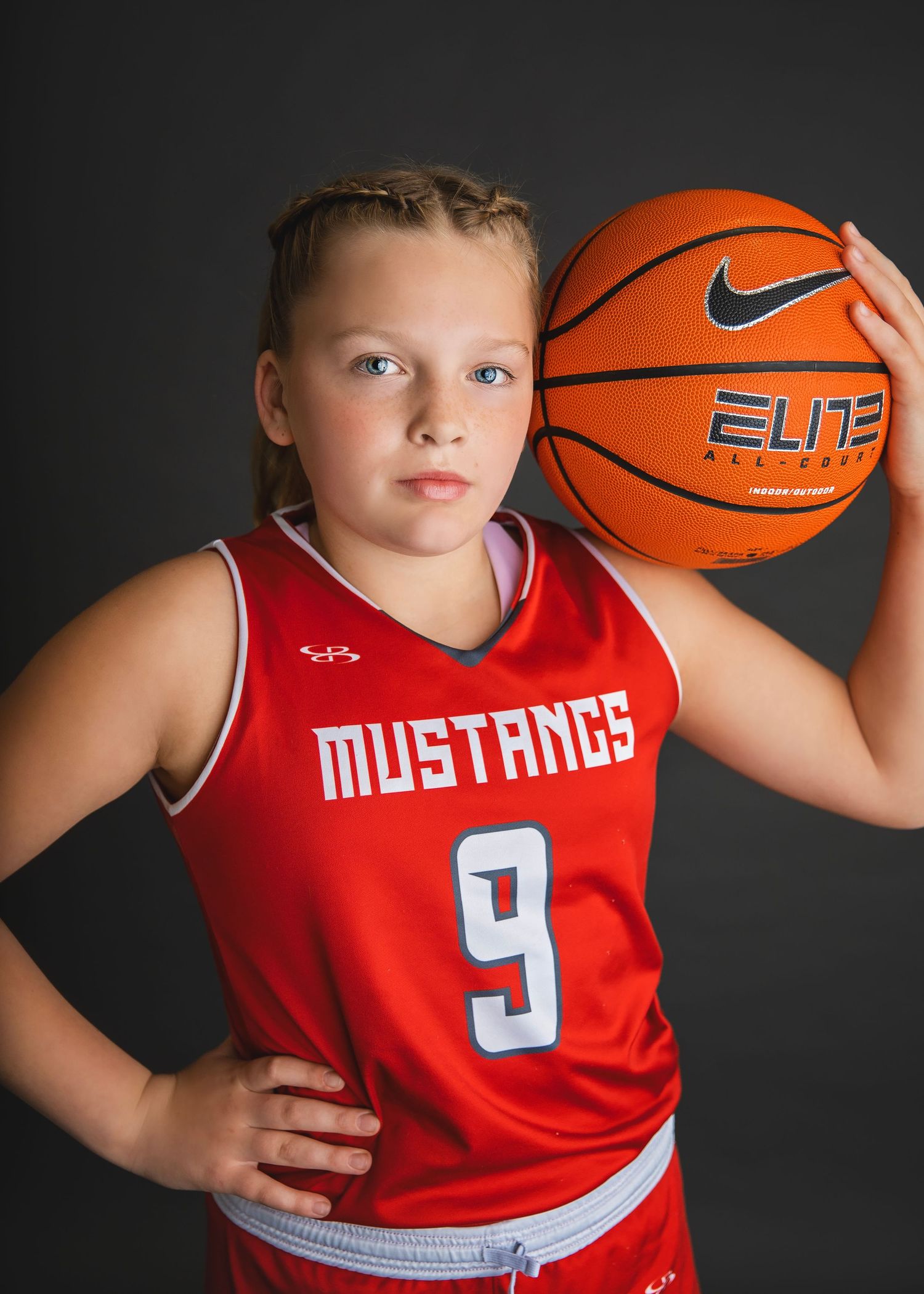 Young player in Mustangs number 9 red jersey holds a Nike Elite basketball confidently.