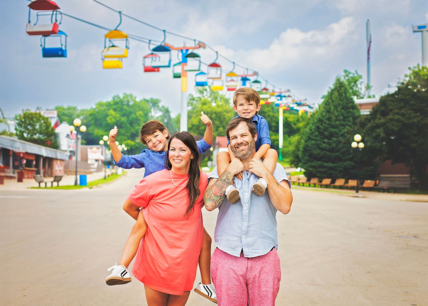 Smiling family of four enjoying a sunny day at an amusement park with colorful sky gondolas.