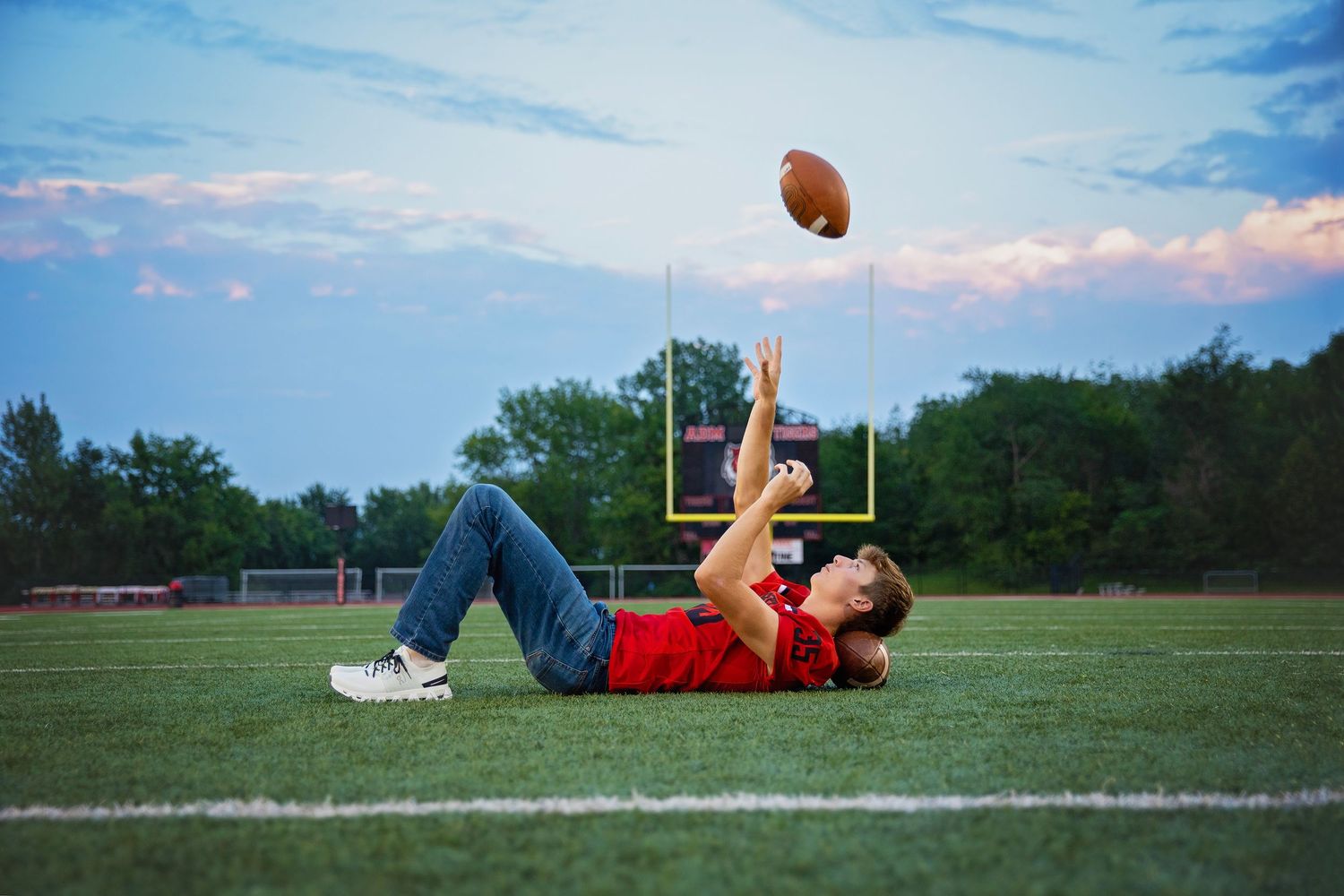 Teenage boy in red shirt lying on football field tossing a football into the air.