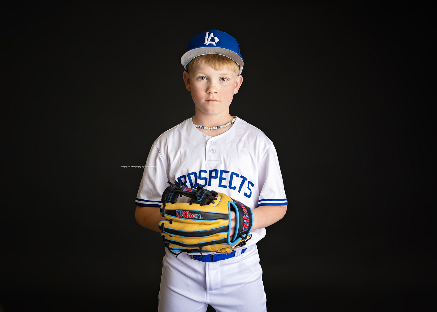 Young boy in Prospects baseball uniform holding glove on black background.