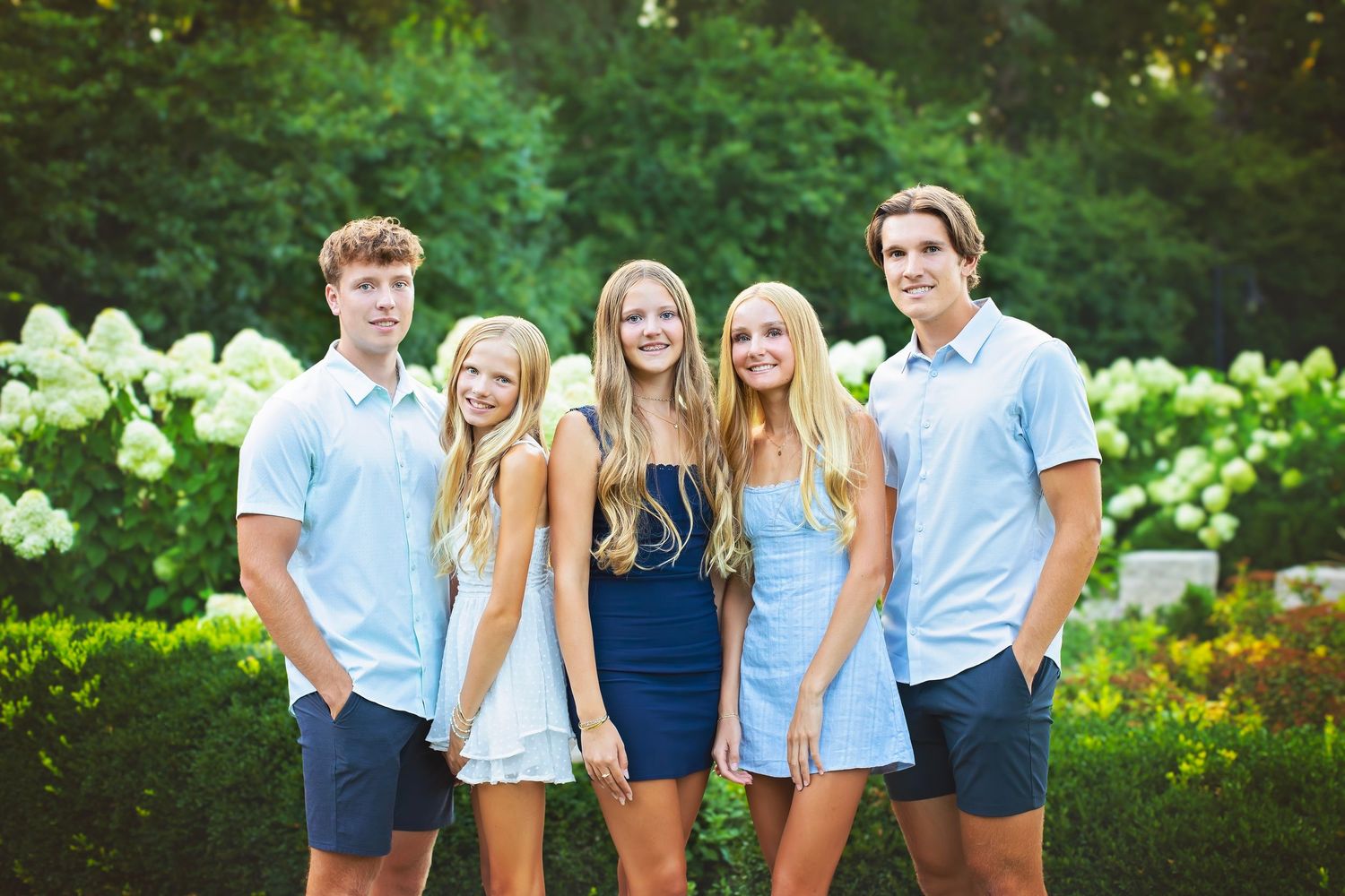 Five teens pose together in front of white hydrangea bushes for a family photo.