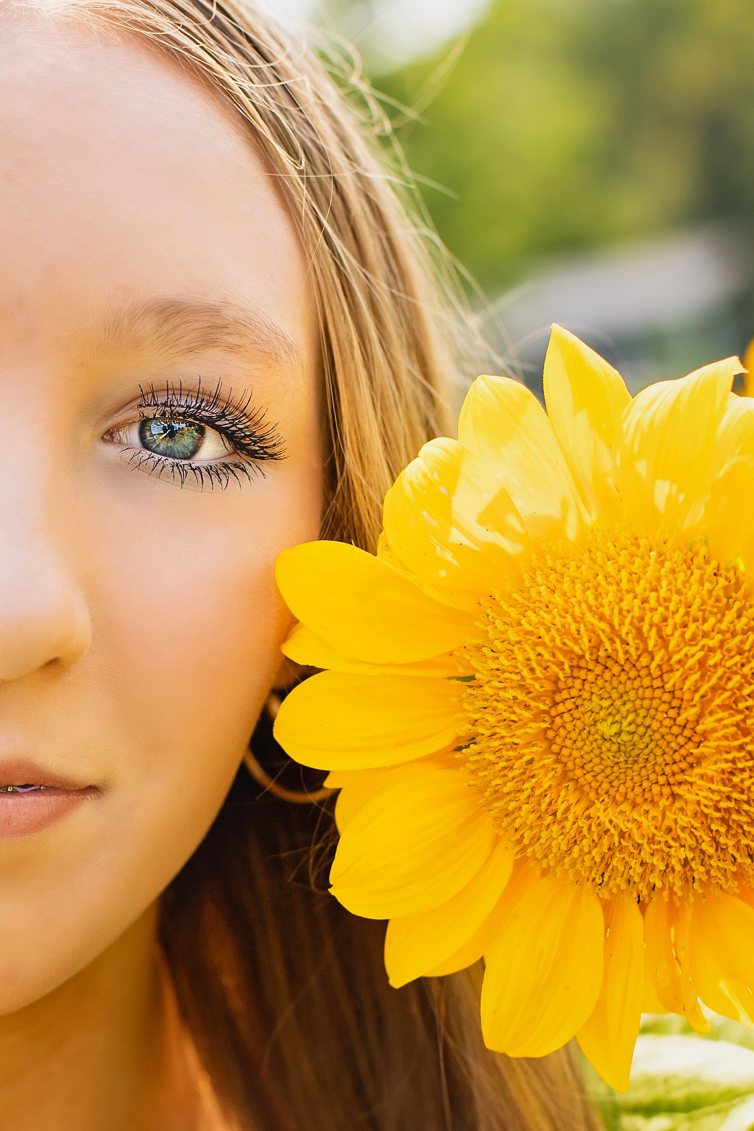 Close-up portrait of teenage girl with blue eyes holding a bright yellow sunflower near her face.