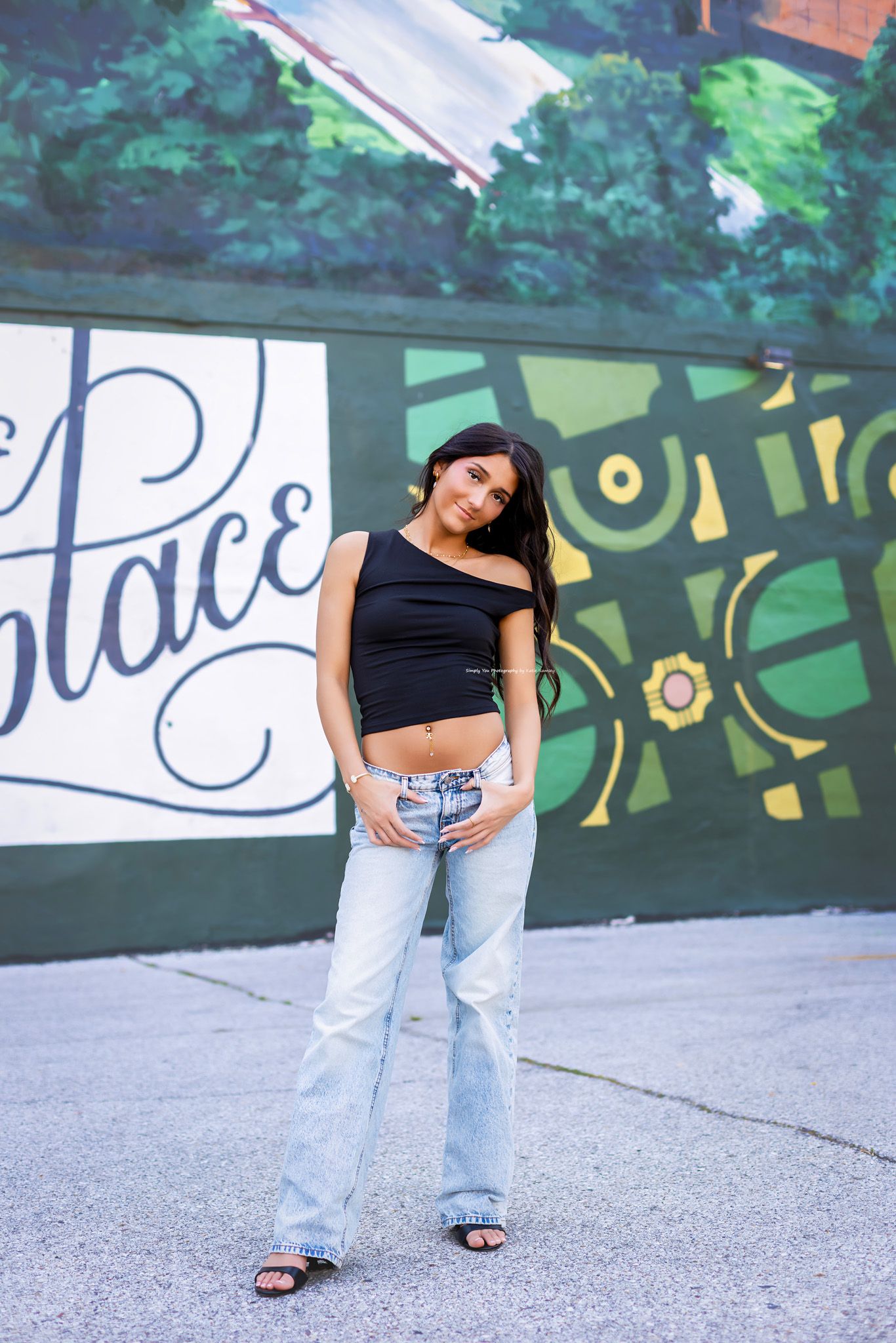 Young woman in black crop top and light blue flare jeans posing in front of a colorful urban mural.