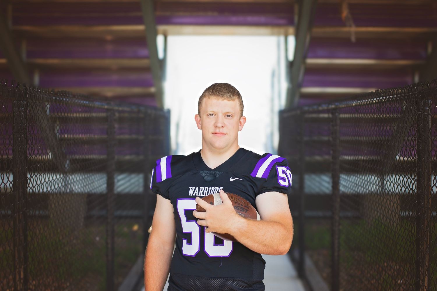 Waukee Warriors football player number 50 walking through stadium tunnel holding a football.
