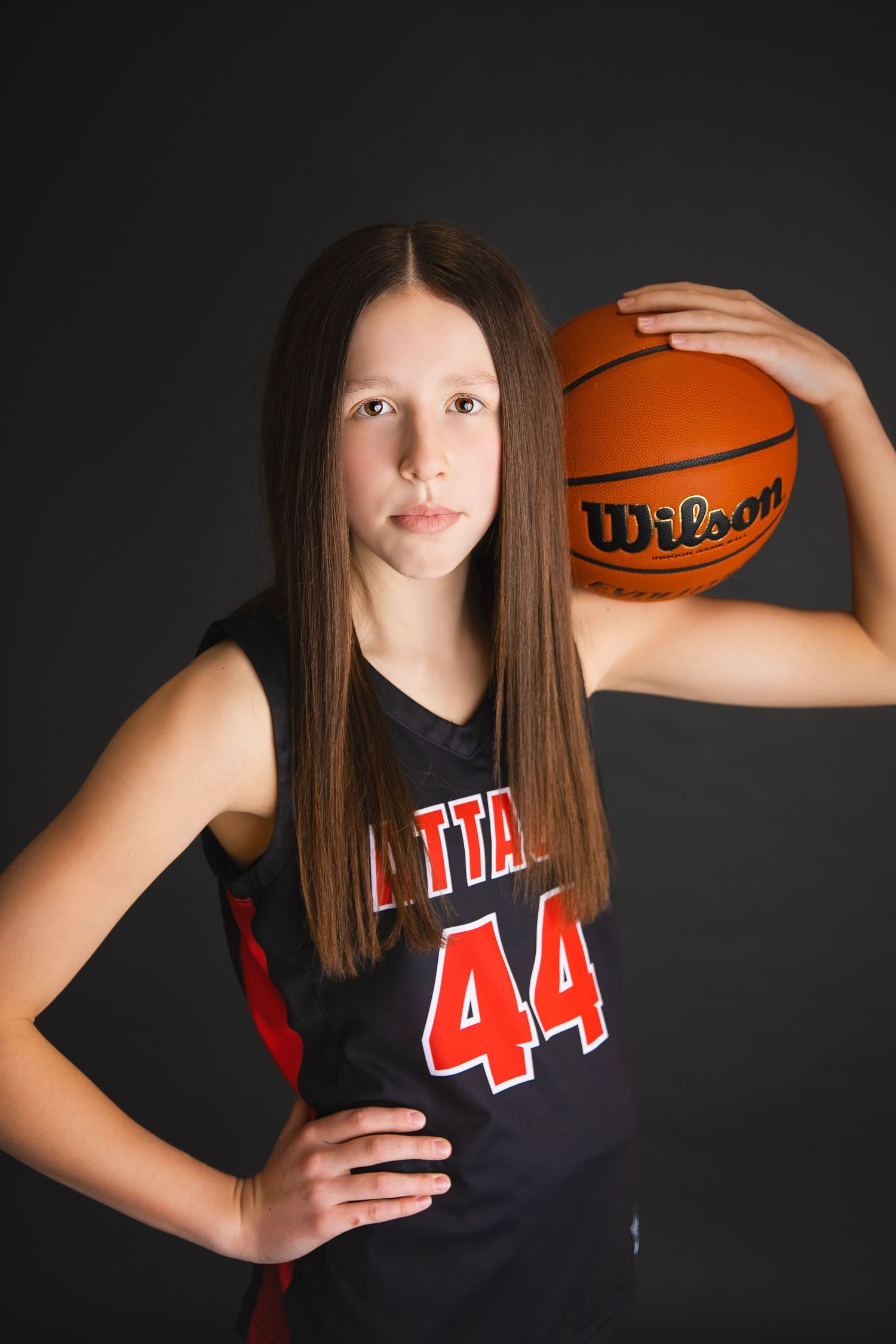 Young girl in number 44 Attack jersey holds a Wilson basketball on her shoulder.