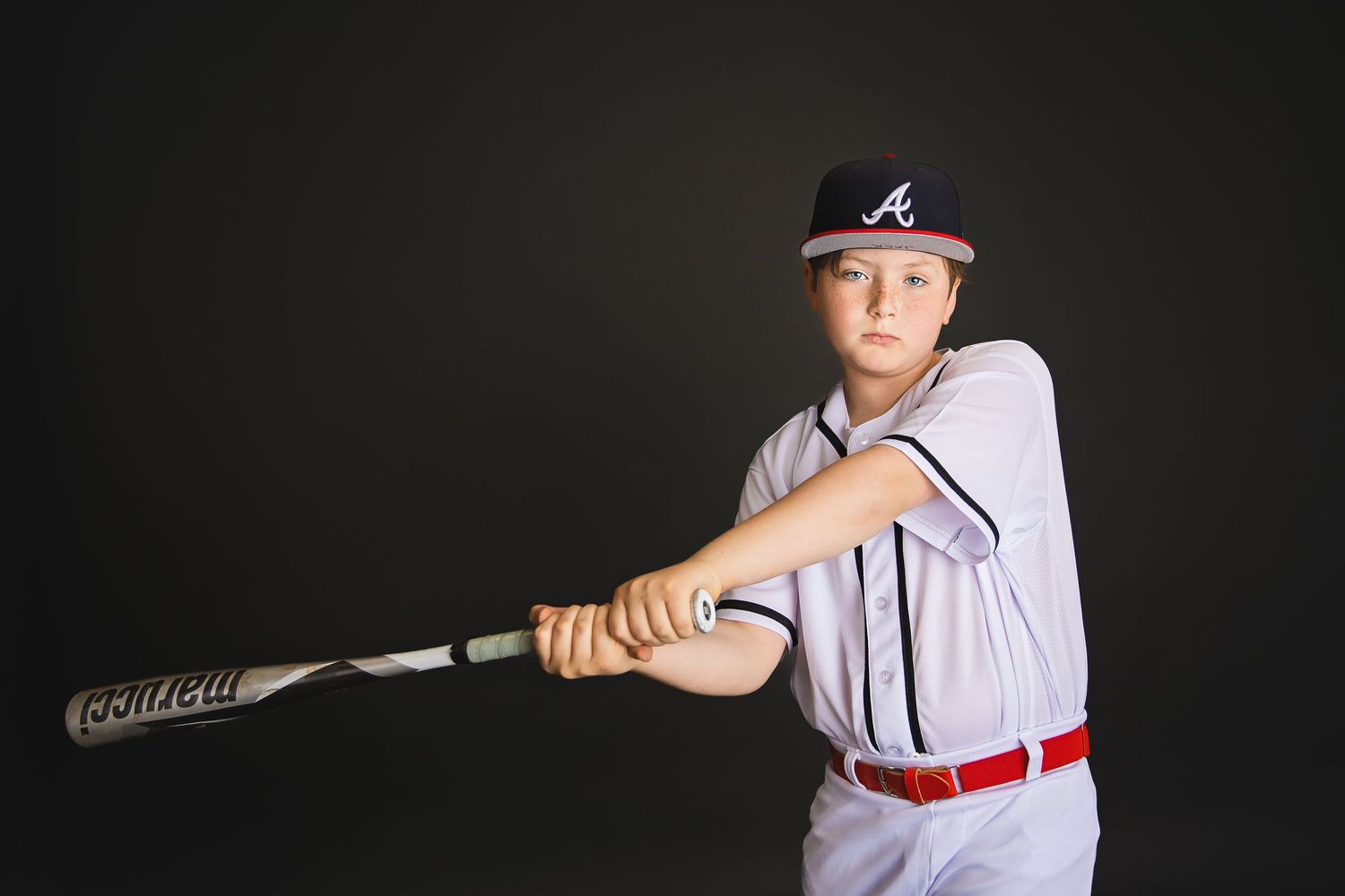 Young baseball player in Braves uniform in batting stance swinging Easton bat, dark studio background.