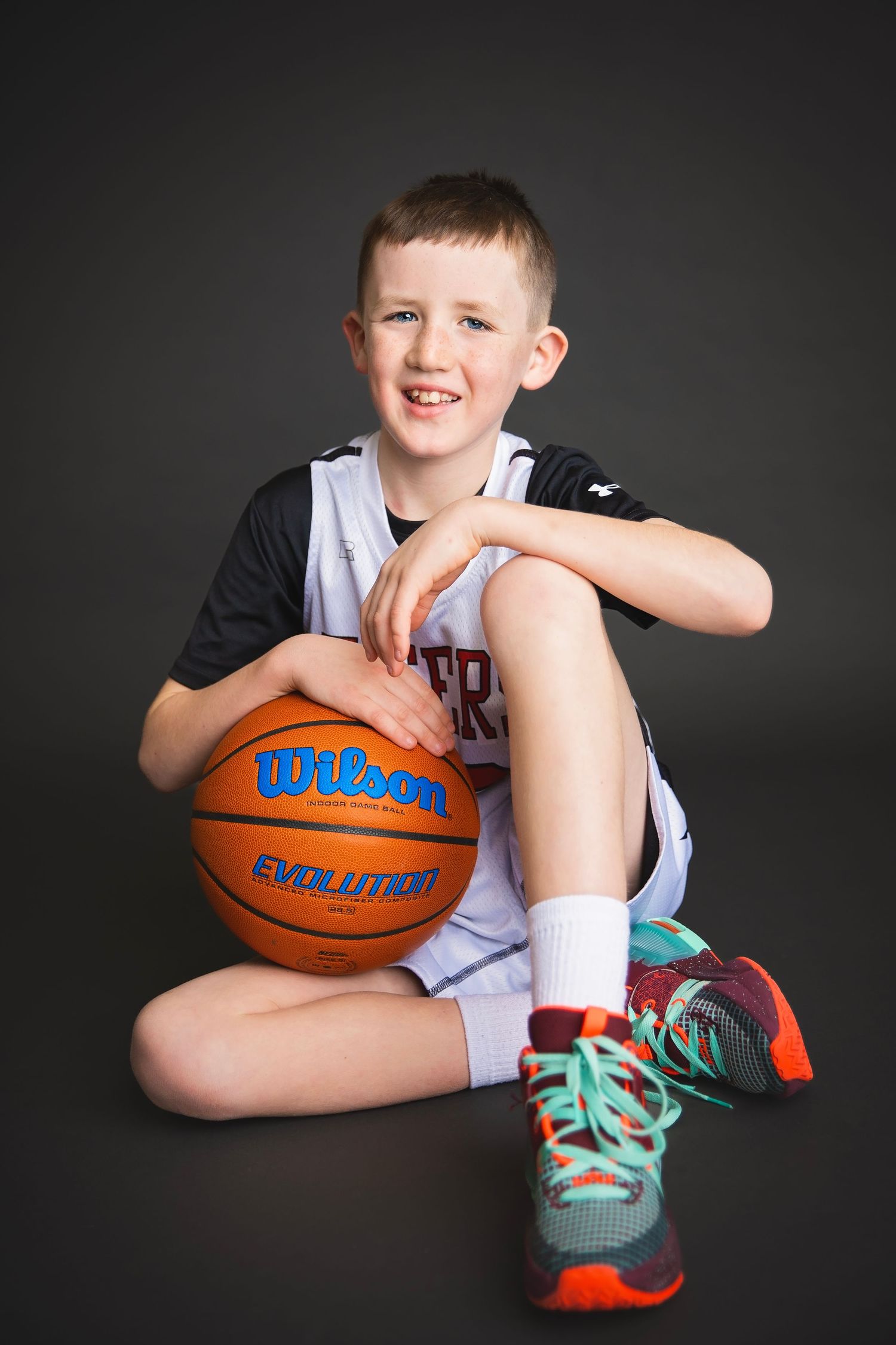 Young boy in Tigers basketball uniform sits smiling with Wilson Evolution basketball.