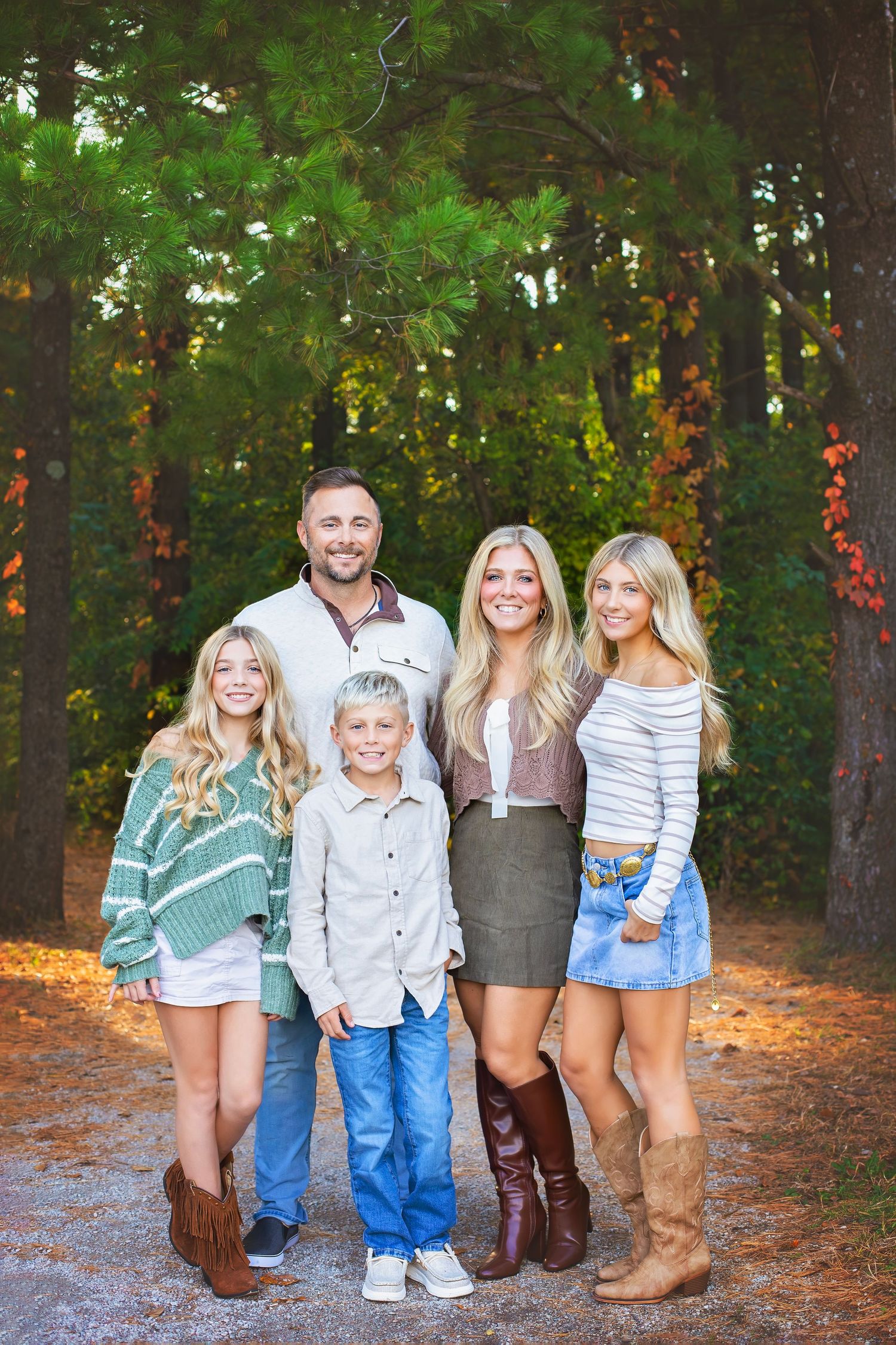 Family of five posing on a pine tree-lined path during fall season.