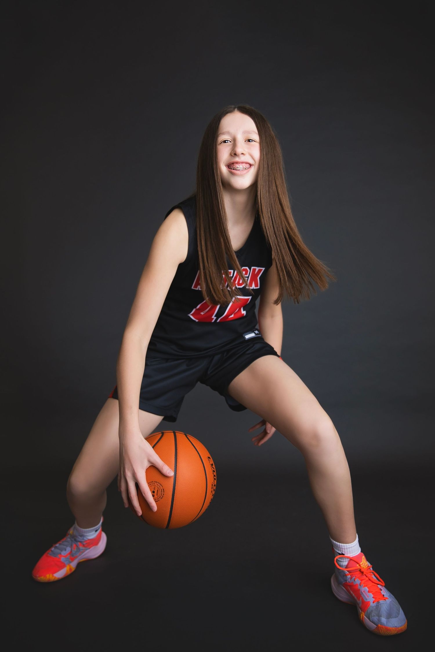 Laughing girl in Attack number 44 jersey dribbles a basketball in a studio setting.