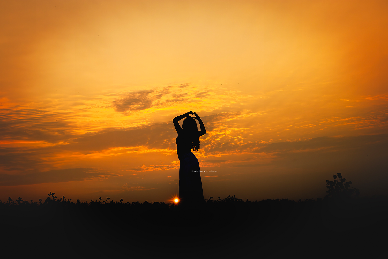 Silhouette of a woman posing gracefully against a vibrant orange sunset sky with dramatic clouds.