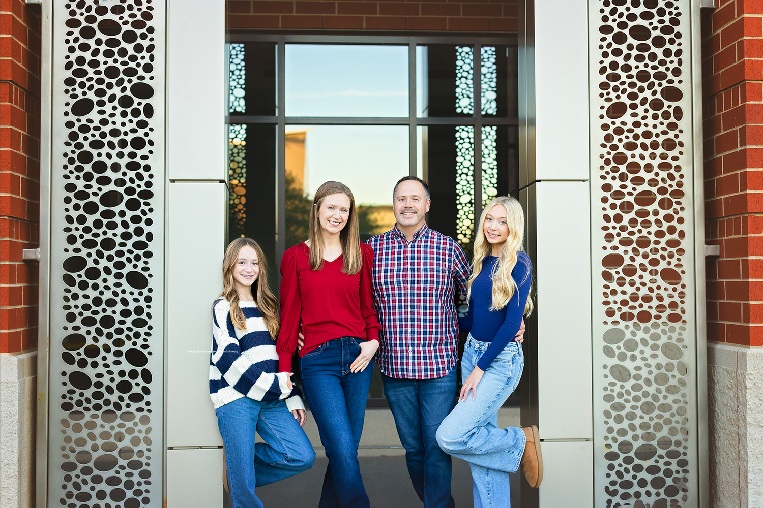 Family of four smiling together in front of an elegant brick building with decorative metal panels.
