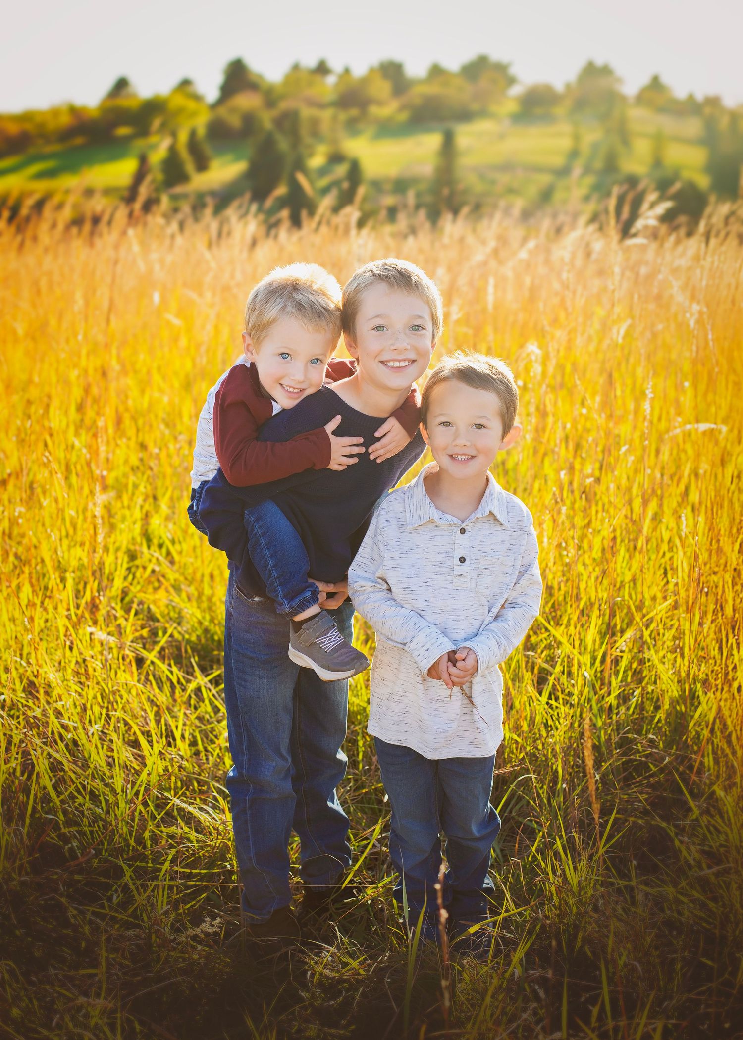 Three young brothers posing together in a golden sunlit field at sunset.