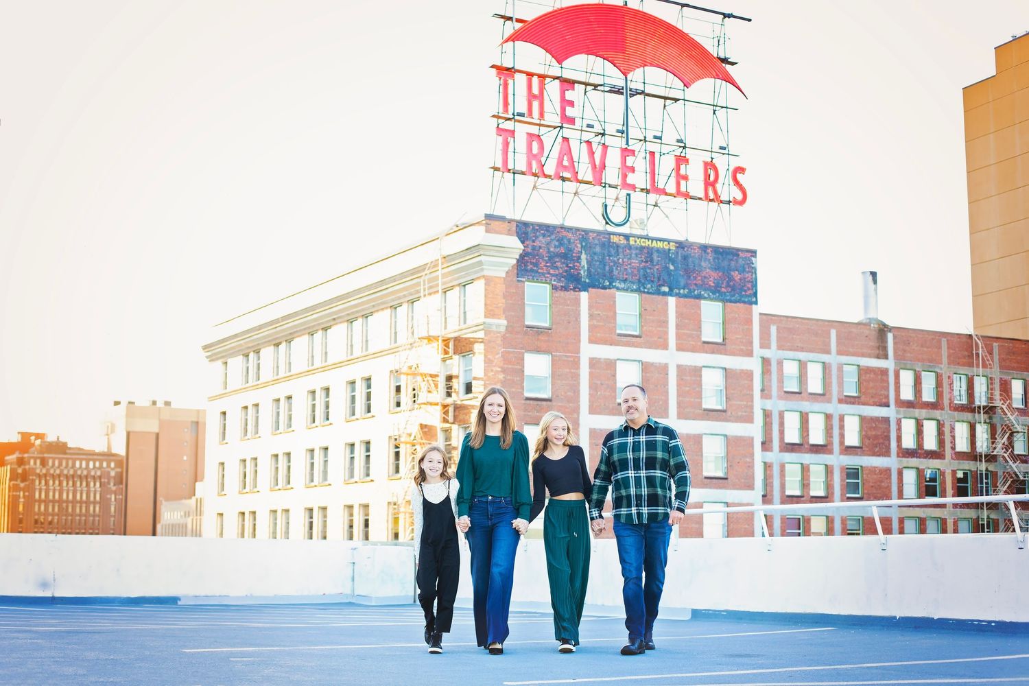 Family of four walking on a rooftop with The Travelers neon sign behind them.