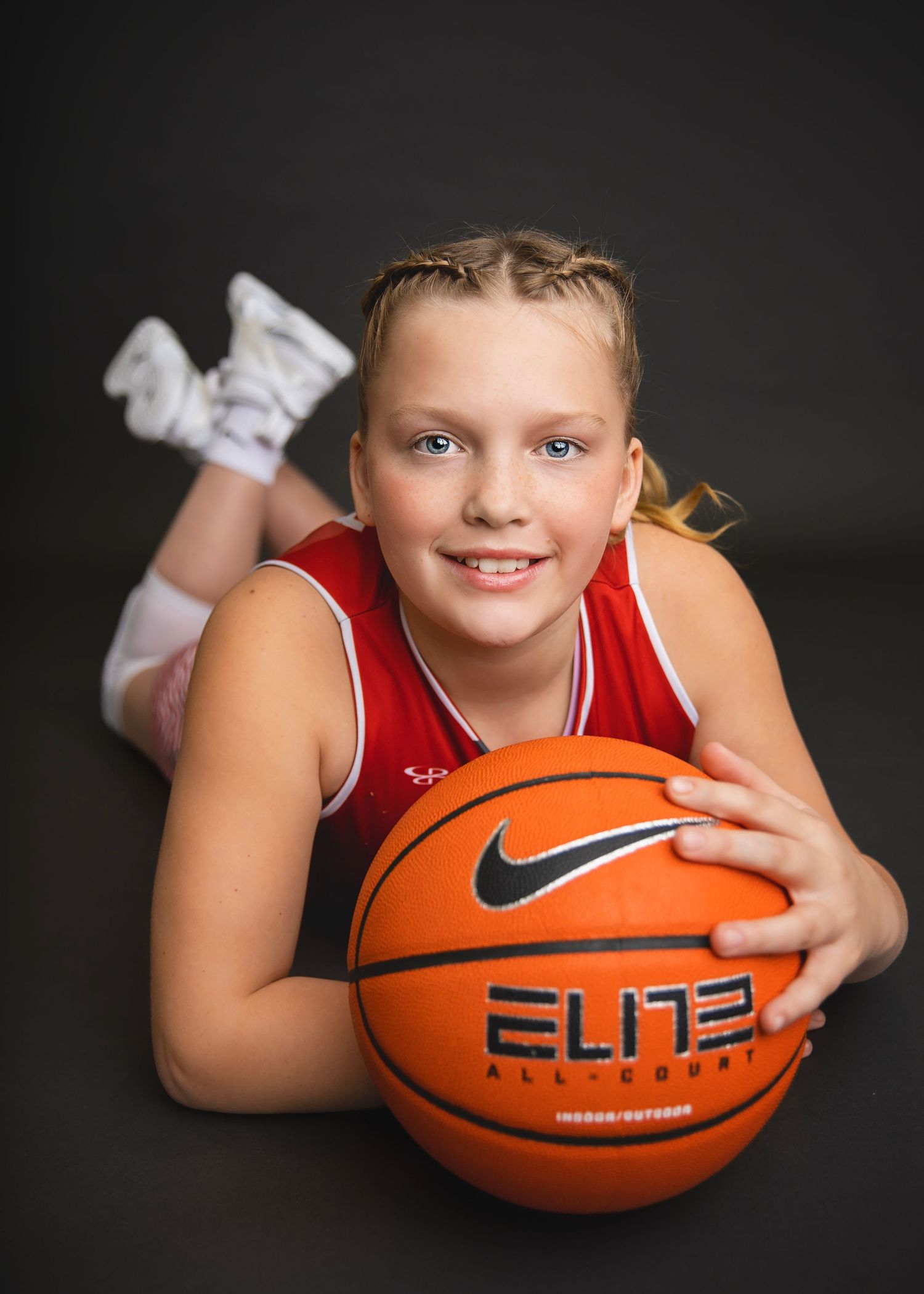 Young girl in red Mustangs basketball uniform lying down smiling with Nike Elite basketball.