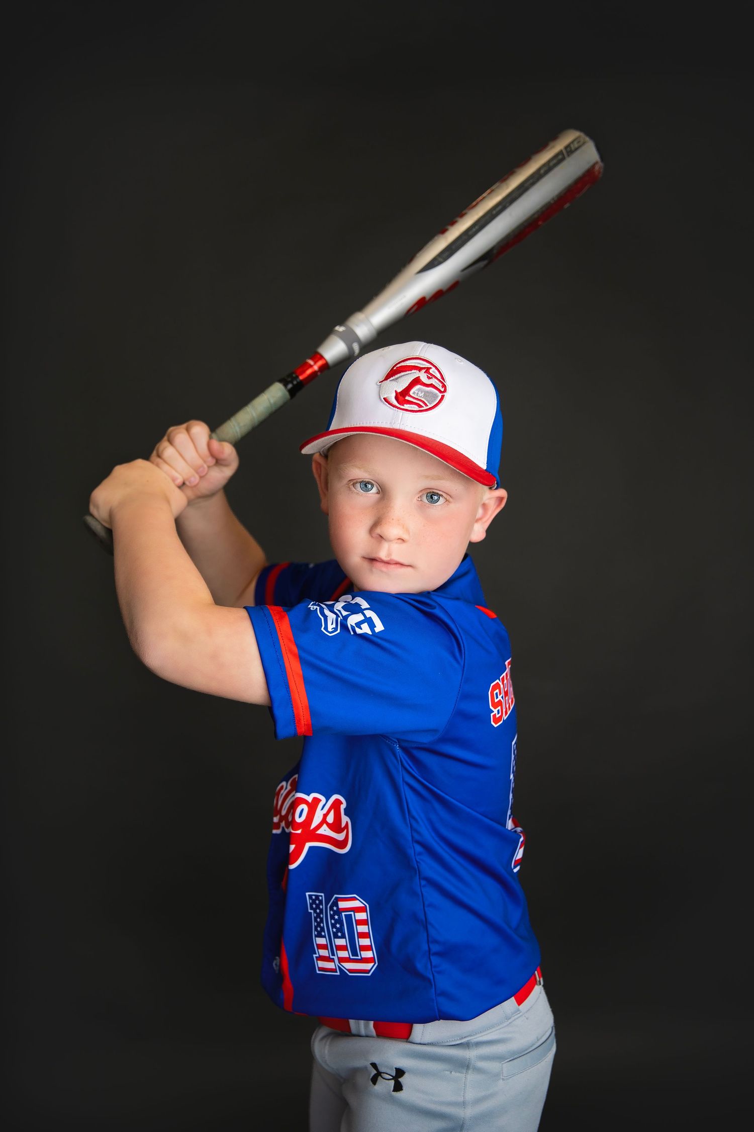 Young boy in blue Mustangs baseball uniform in batting stance holding silver bat in studio.