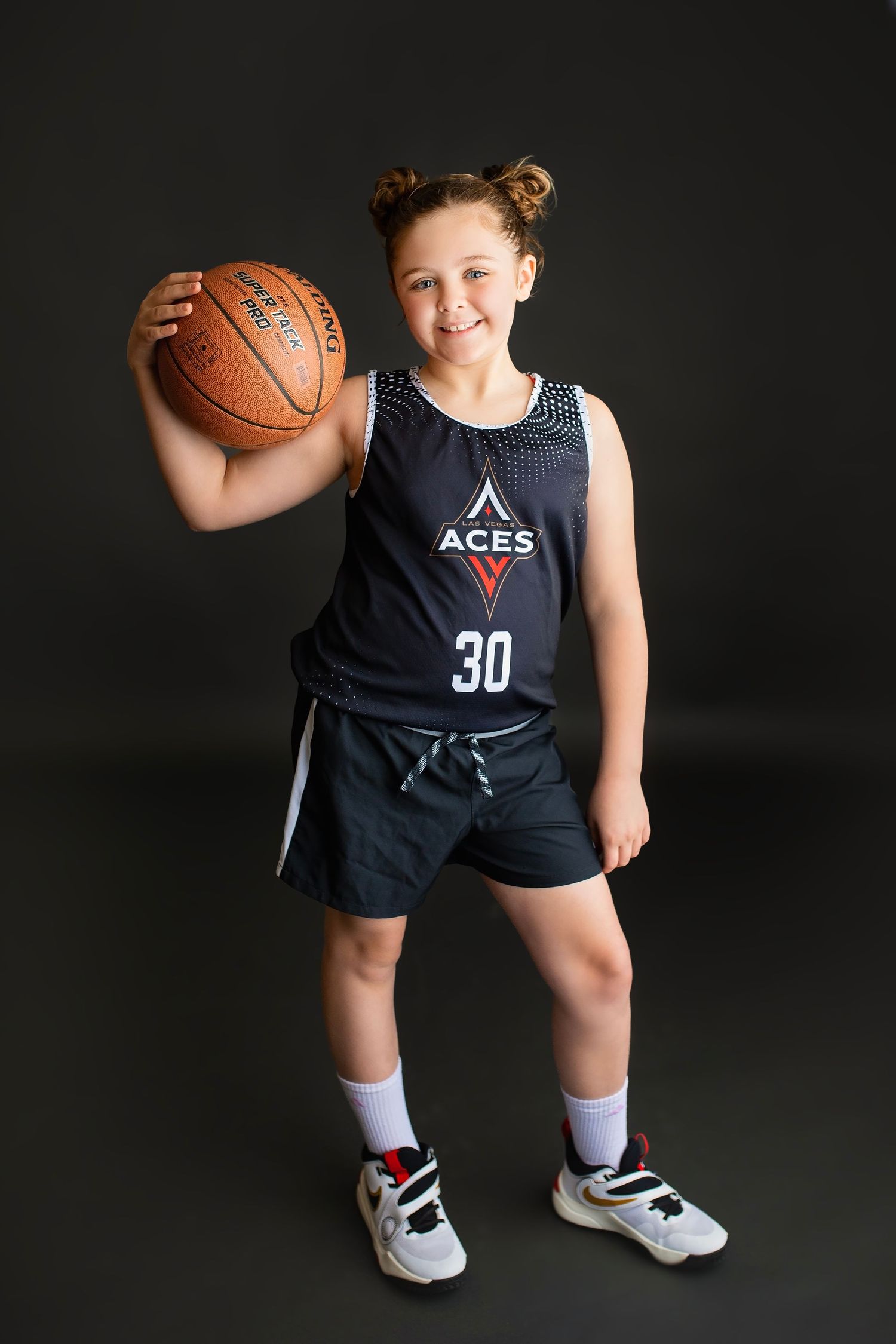Young girl in Aces #30 basketball jersey holding a ball, smiling for a sports team photo.
