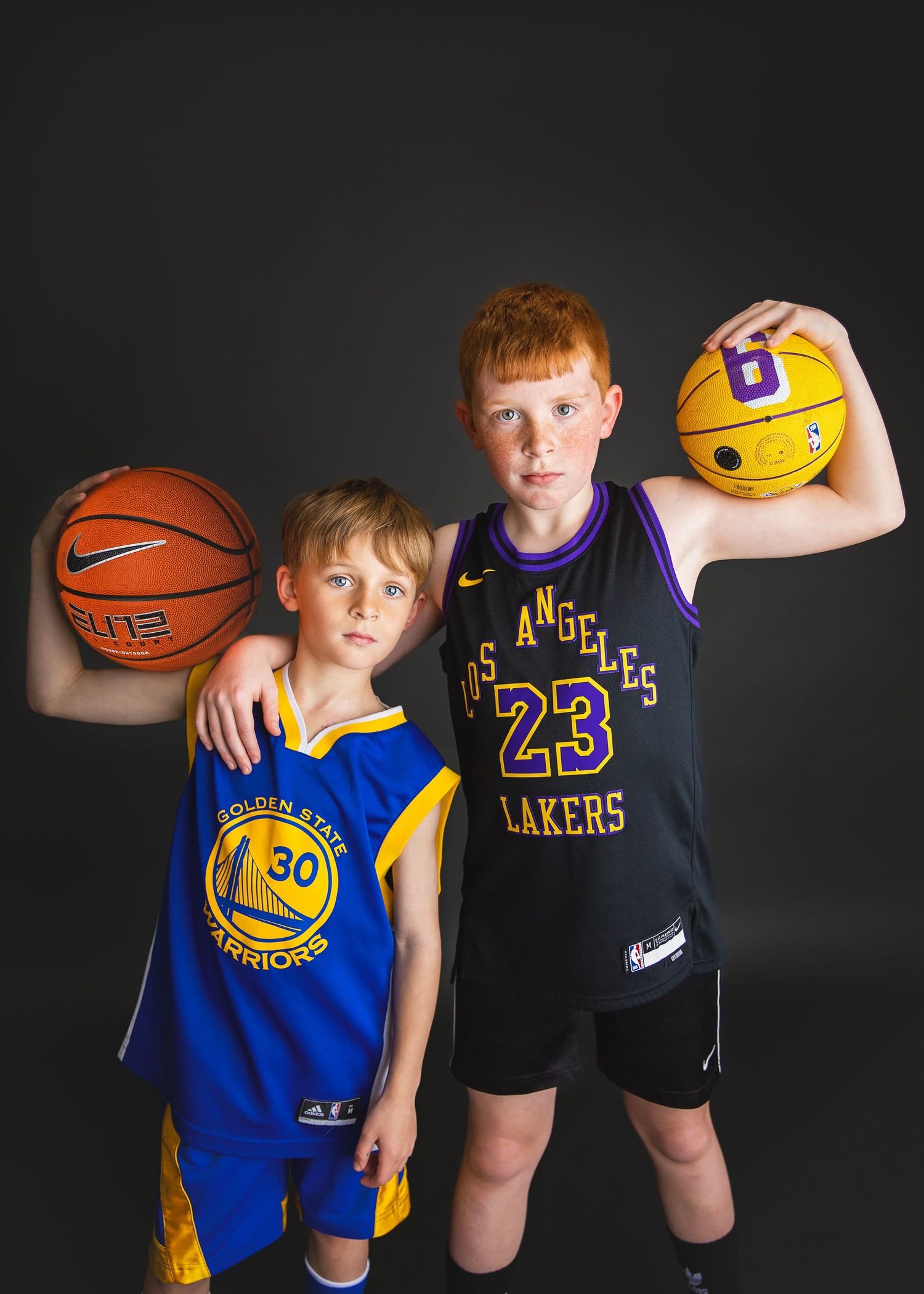 Two boys in NBA jerseys pose with basketballs, Warriors and Lakers uniforms.