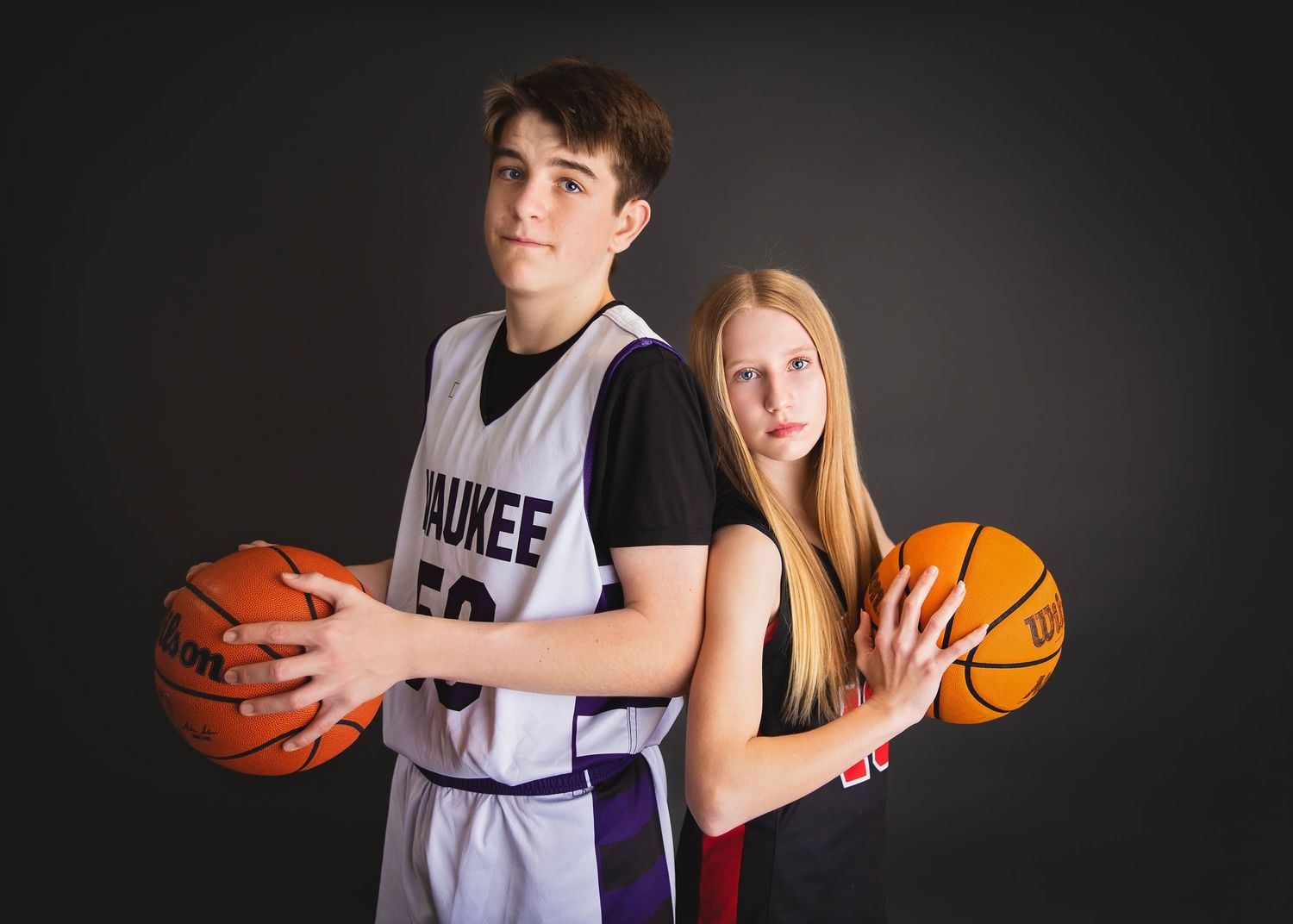 Teen male and female basketball players standing back to back with balls.