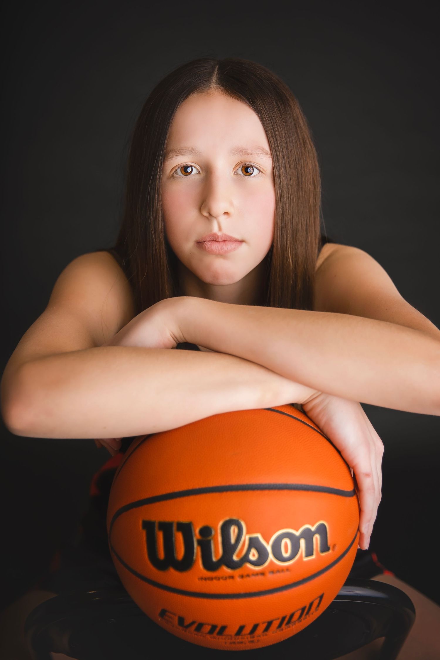 Young girl rests arms on a Wilson Evolution basketball with a serious expression.