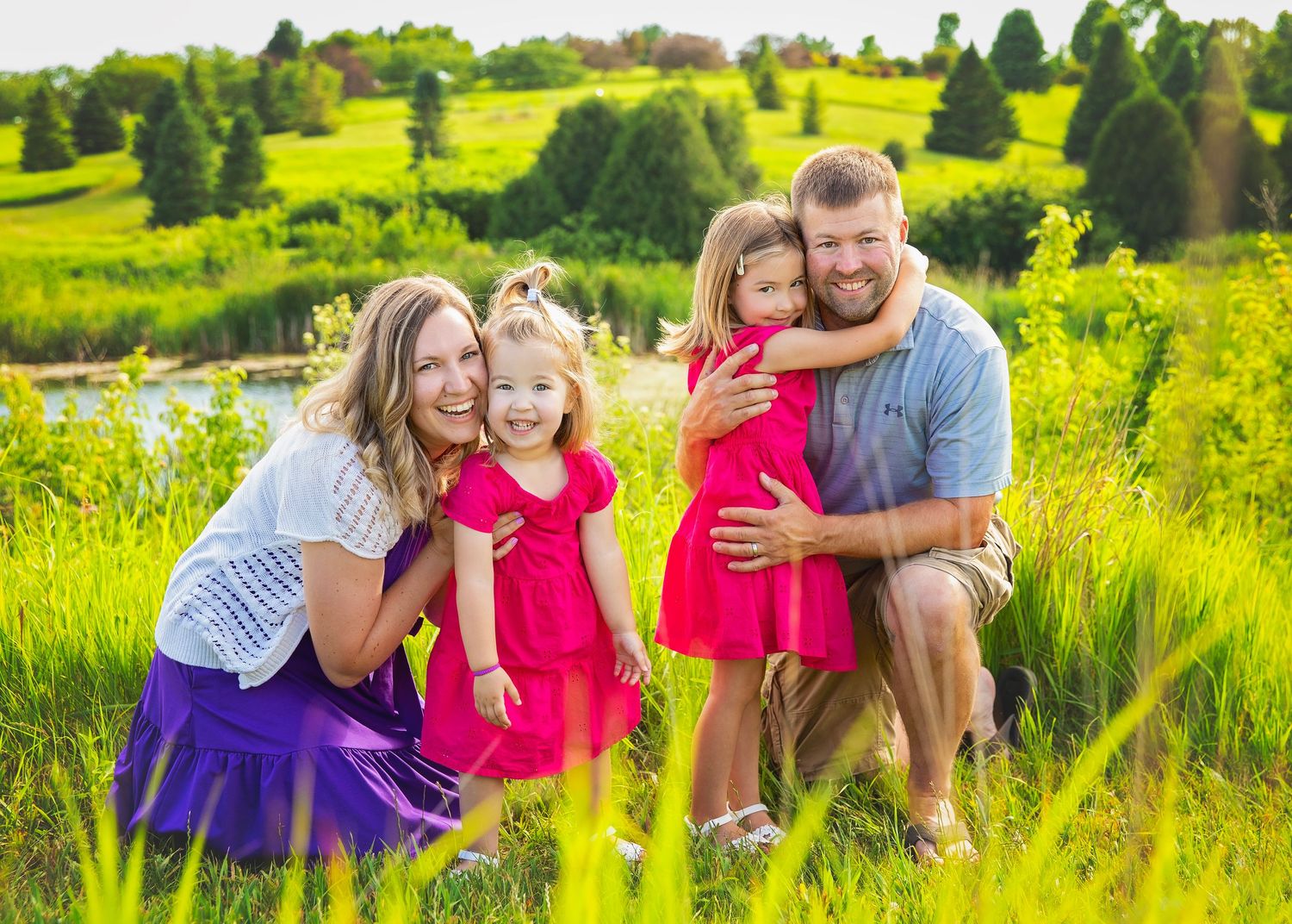 Joyful family of four with two girls in pink dresses laughing in a lush green meadow.