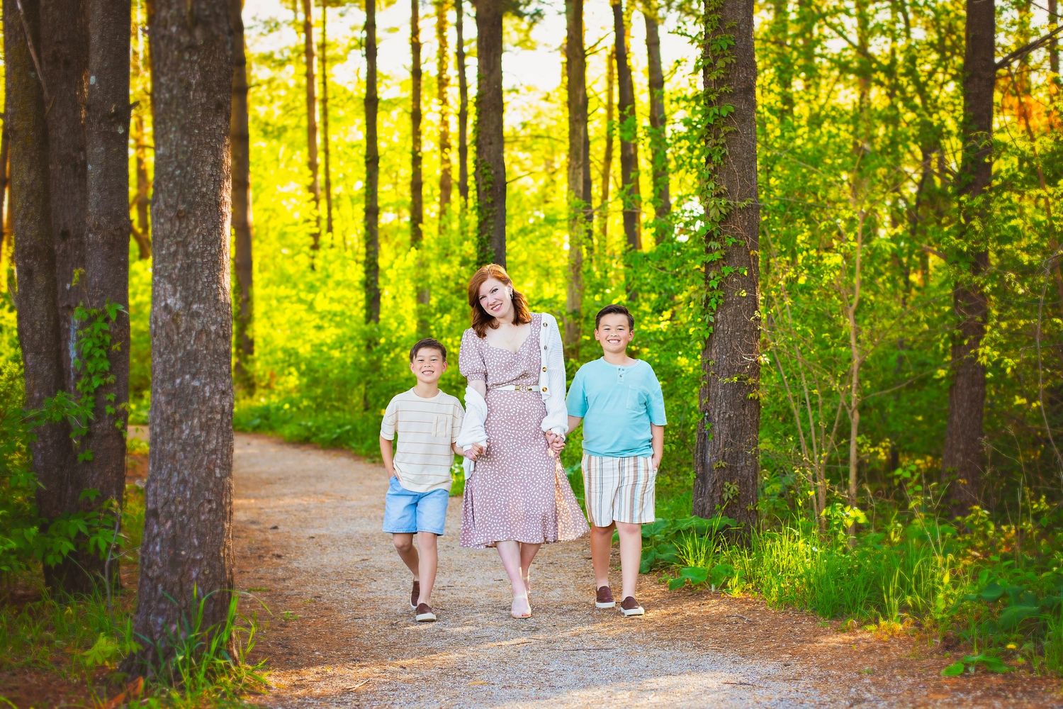 Mother walks hand-in-hand with two boys along a sunlit forest path.