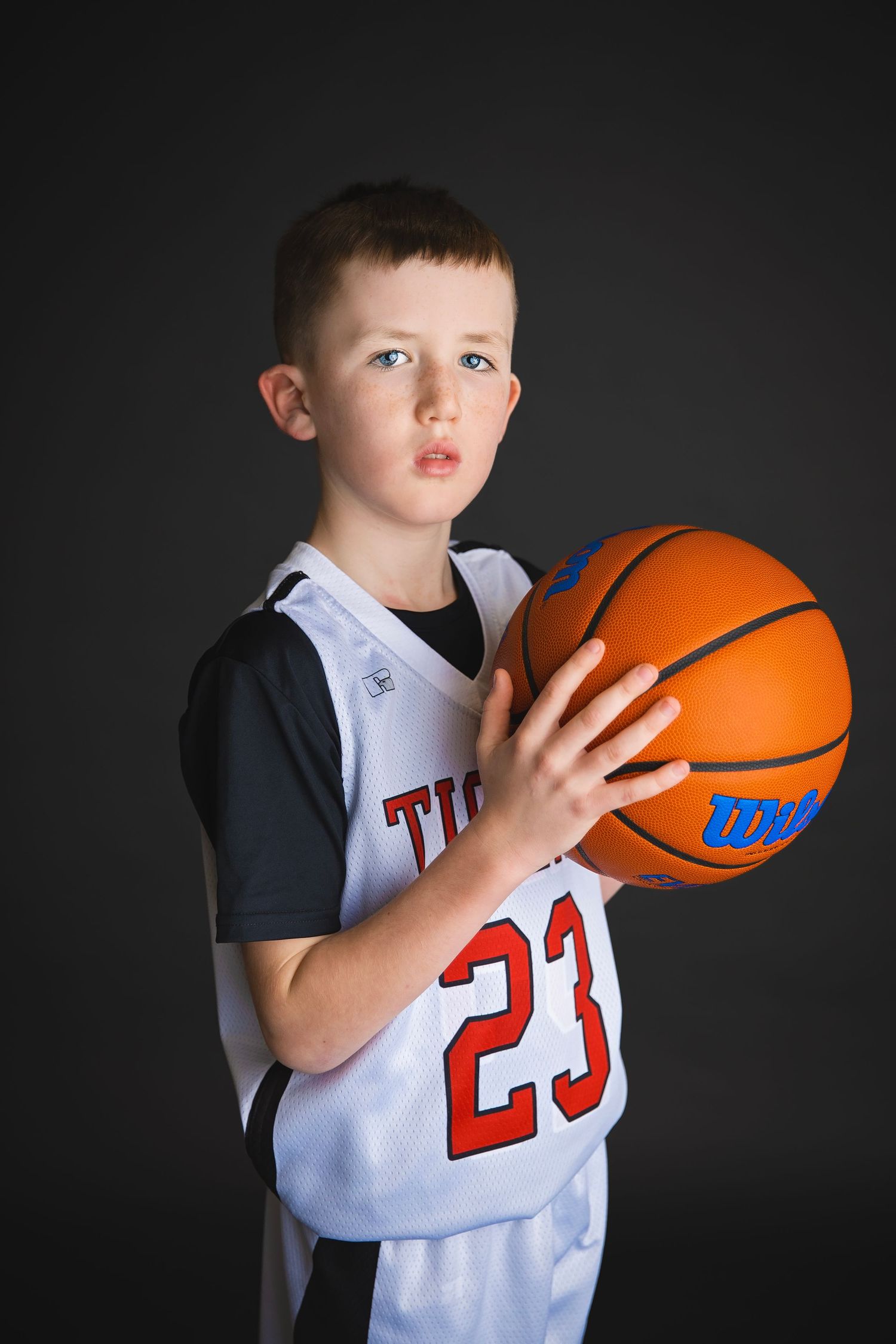 Youth basketball player in Tigers jersey number 23 holds Wilson basketball.