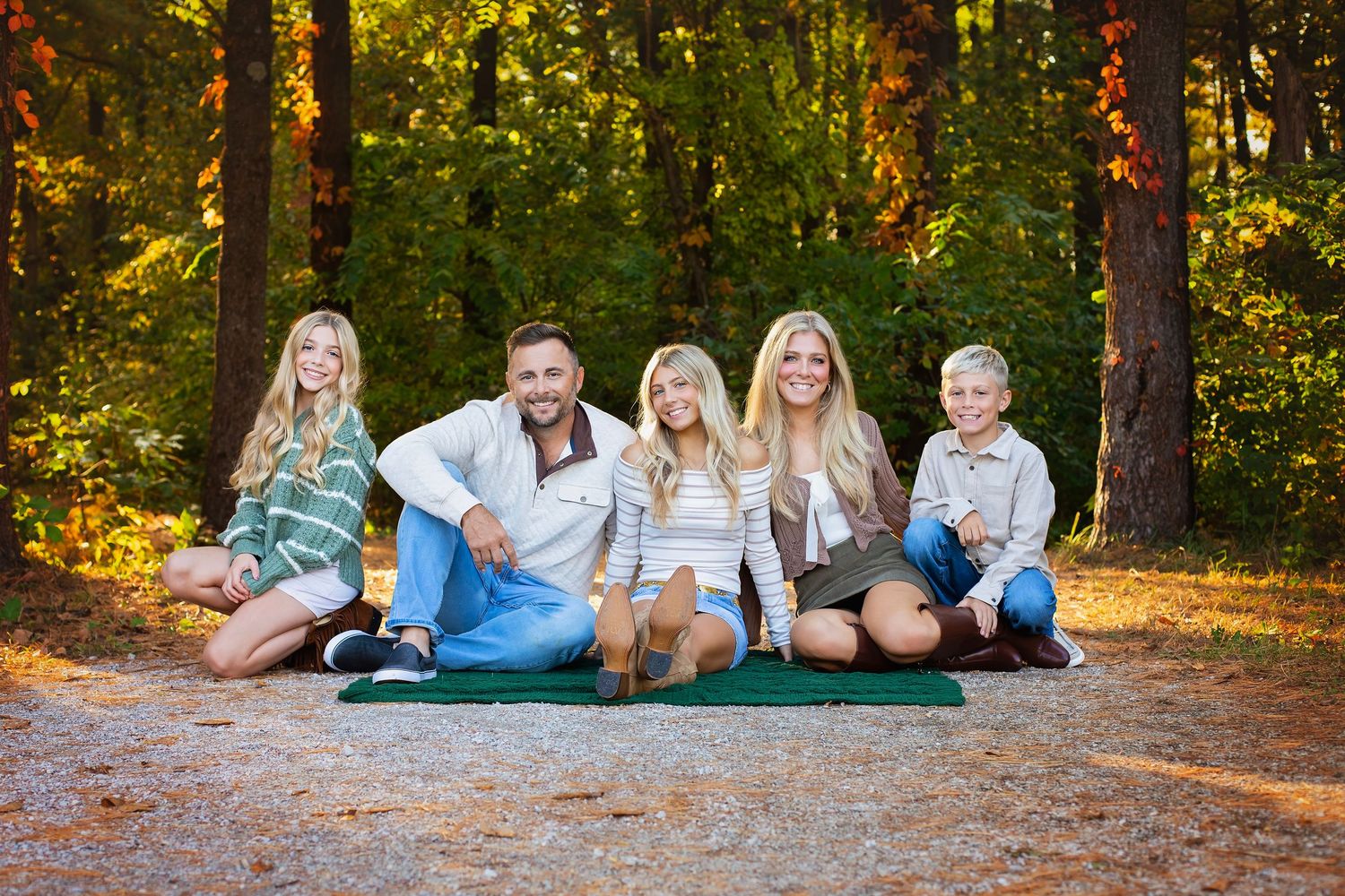 A happy family of five sits together on a forest path surrounded by colorful autumn foliage.
