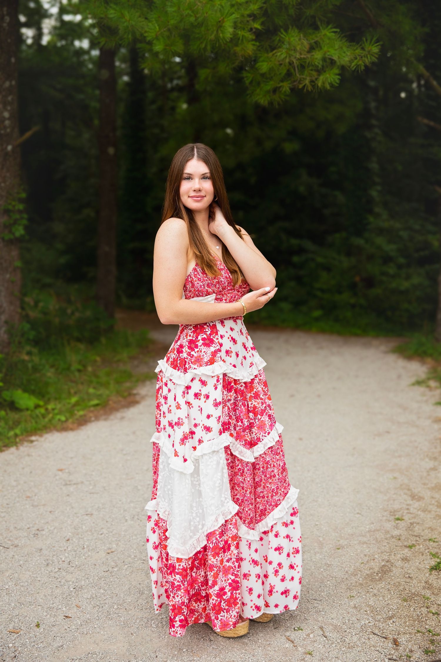 Young woman in red floral maxi dress on gravel path in forest.