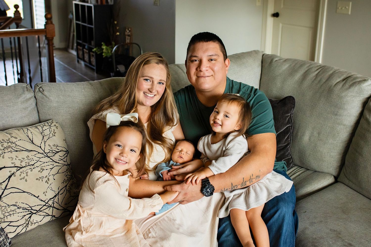 Happy family of five with newborn baby posing together on a gray couch in their home.