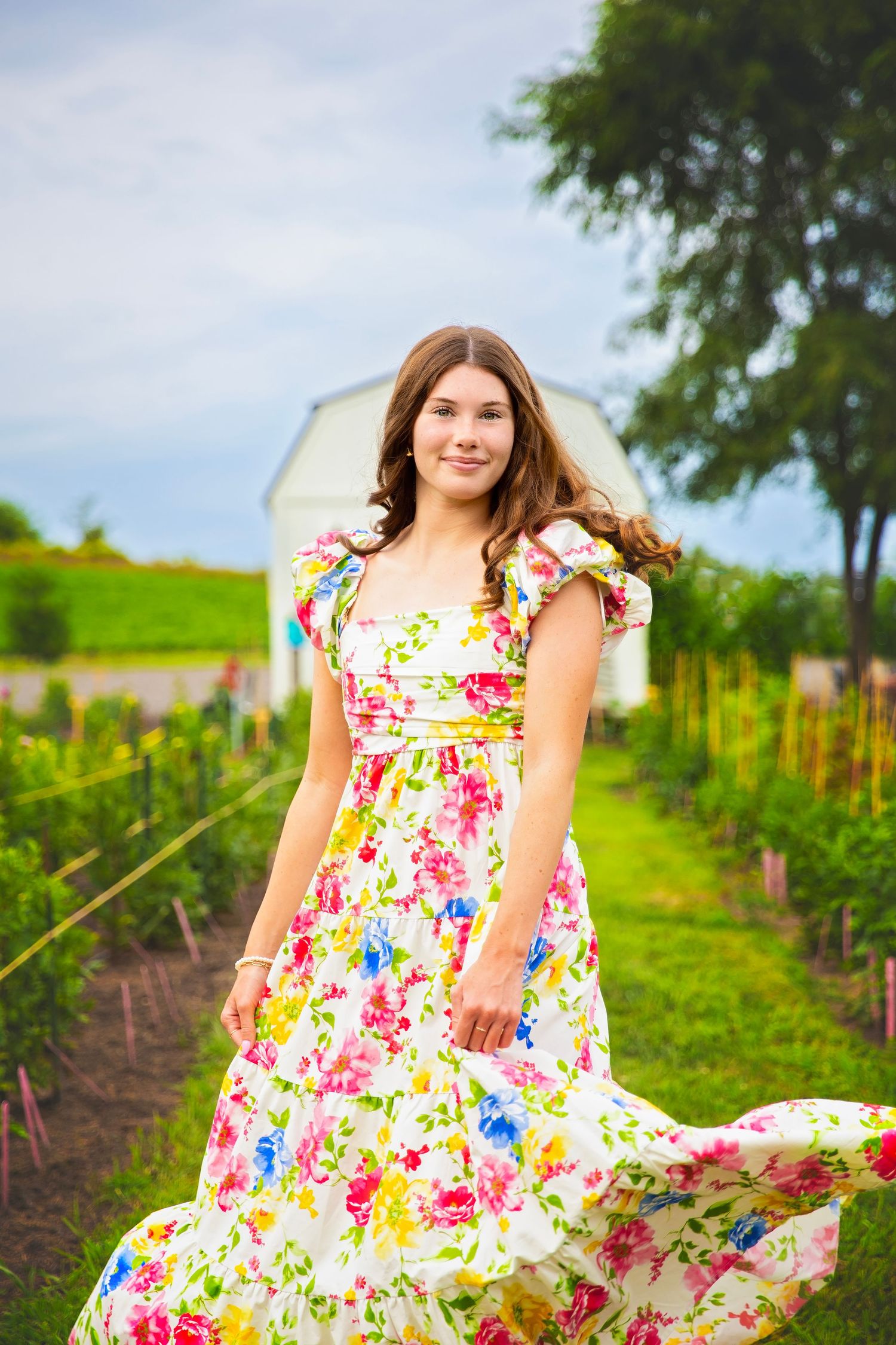 Teen girl twirling in a vibrant floral dress in a garden with a white barn.
