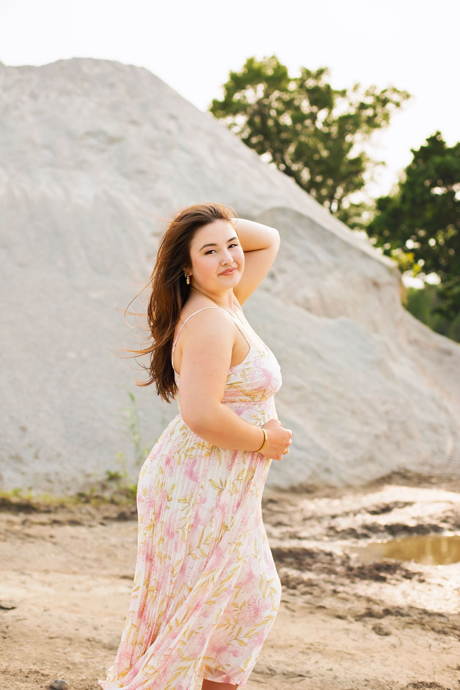 Young woman in floral sundress posing before a large sand dune in golden sunlight.
