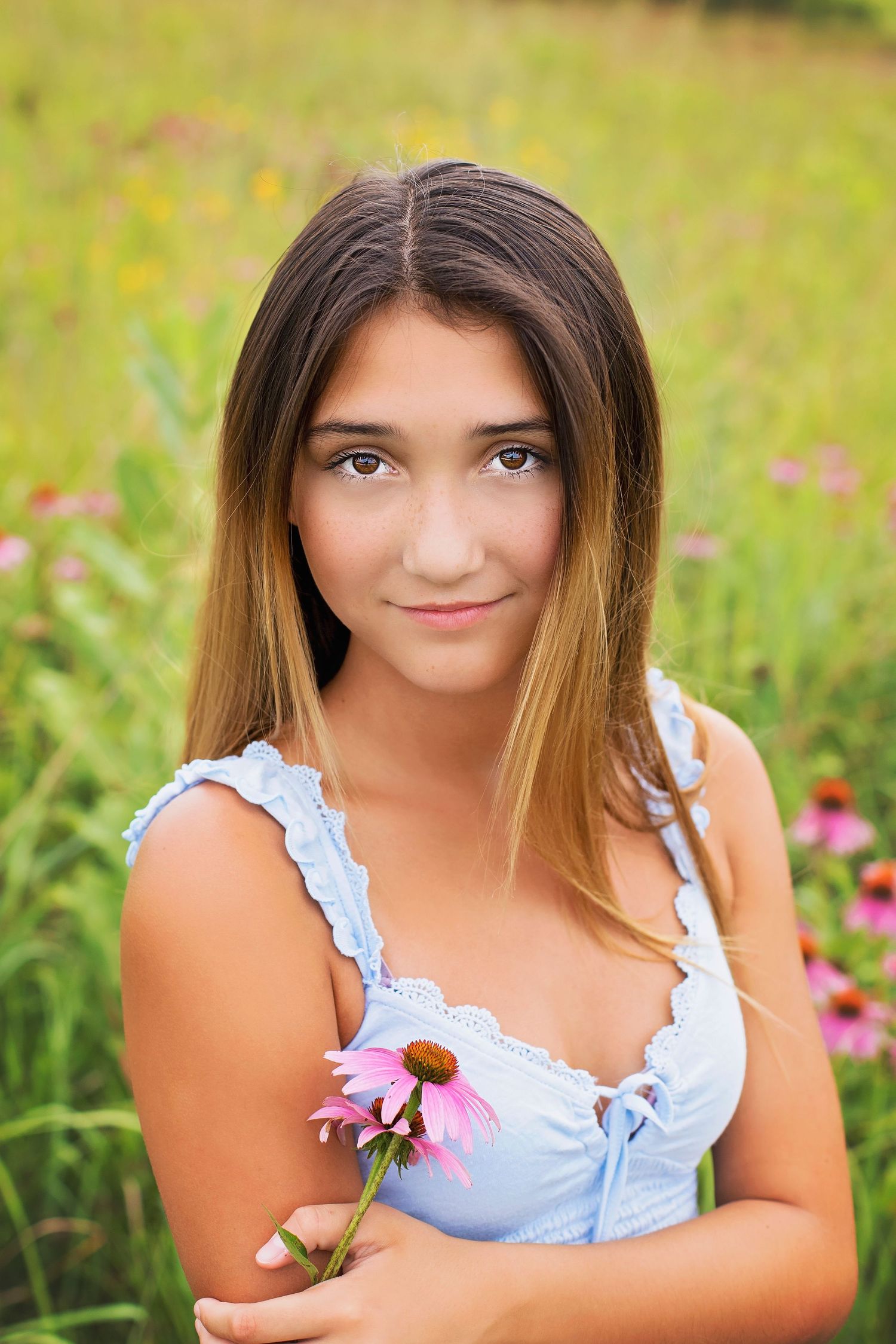 Teen girl in blue dress holding a pink coneflower in a colorful wildflower field.