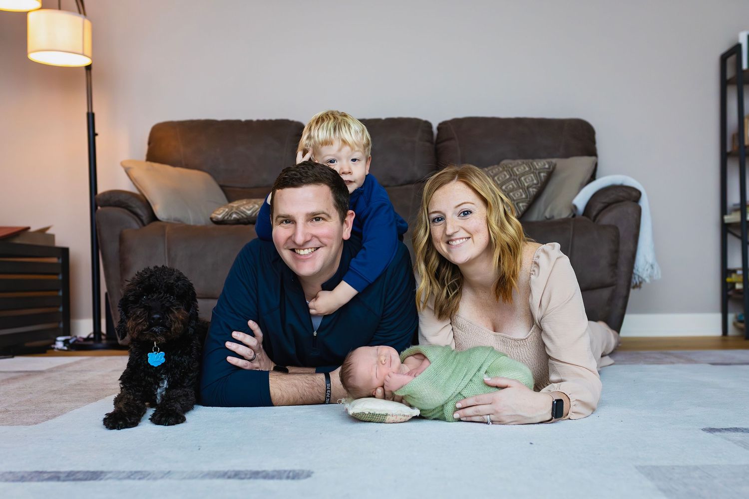 Happy family with two boys and black dog lying on living room floor smiling at camera.