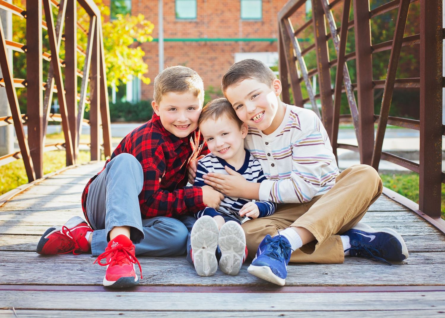 Three young brothers hugging and smiling together on a wooden bridge.