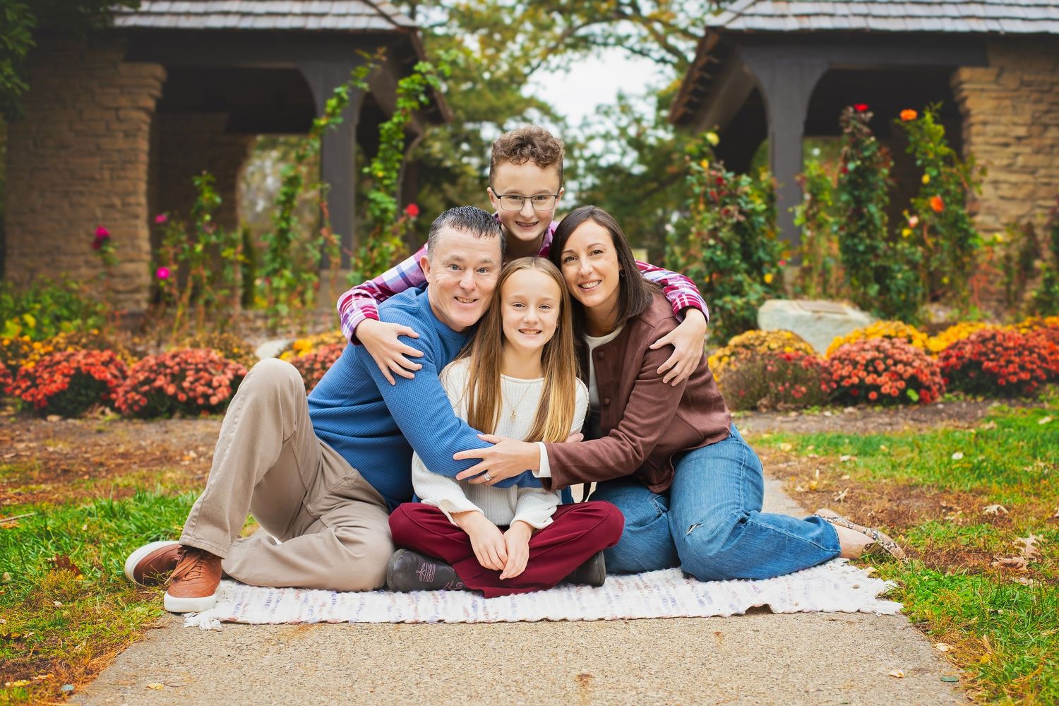 Family of four sitting together on a blanket in a garden with fall flowers.