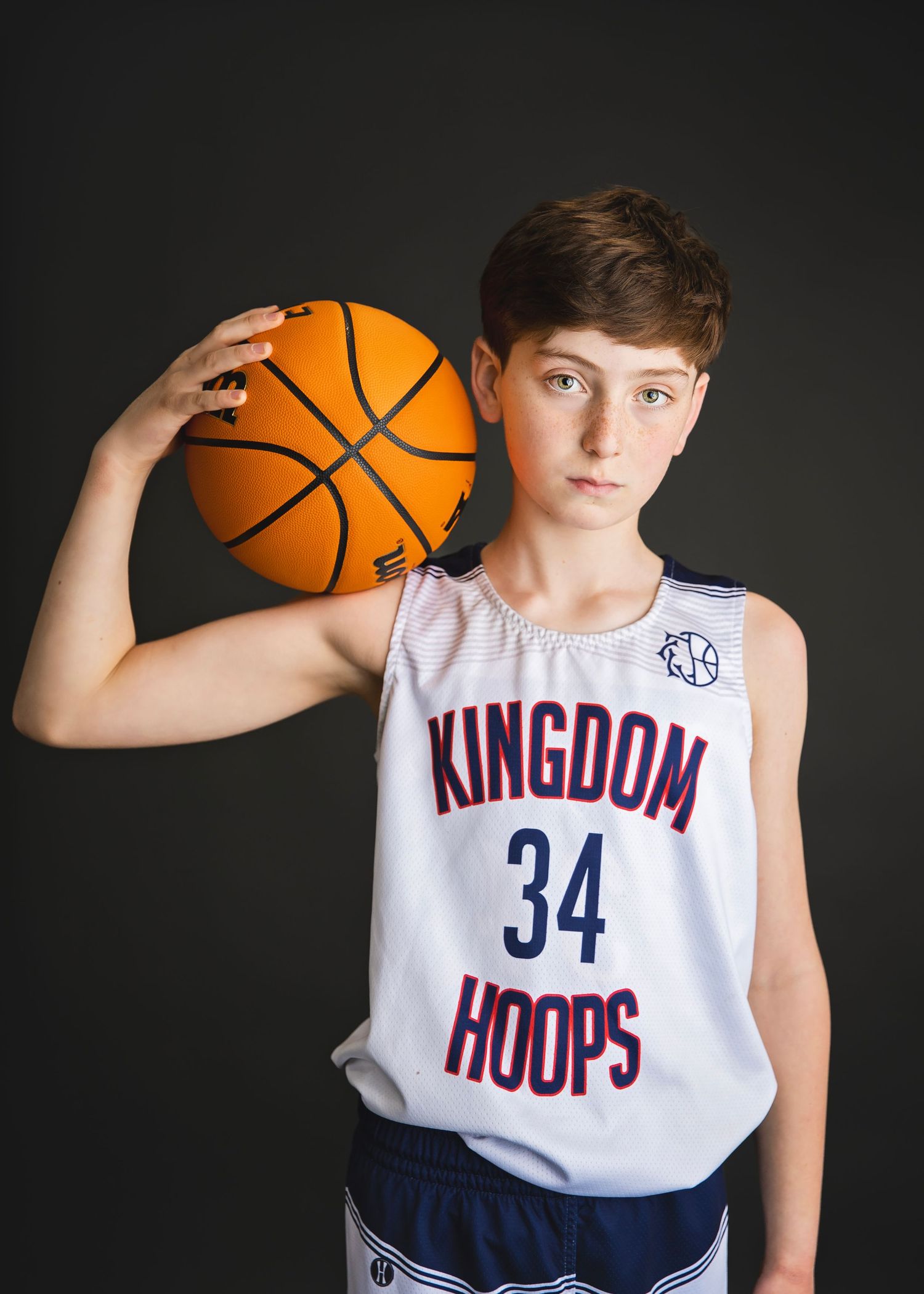Young boy in Kingdom Hoops number 34 jersey holding a basketball on his shoulder.