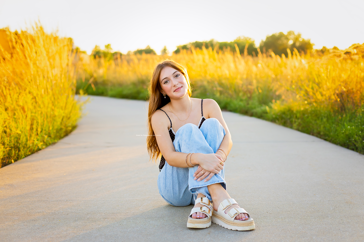 Young woman in blue dress sitting on a path surrounded by golden grasses in warm sunset light.