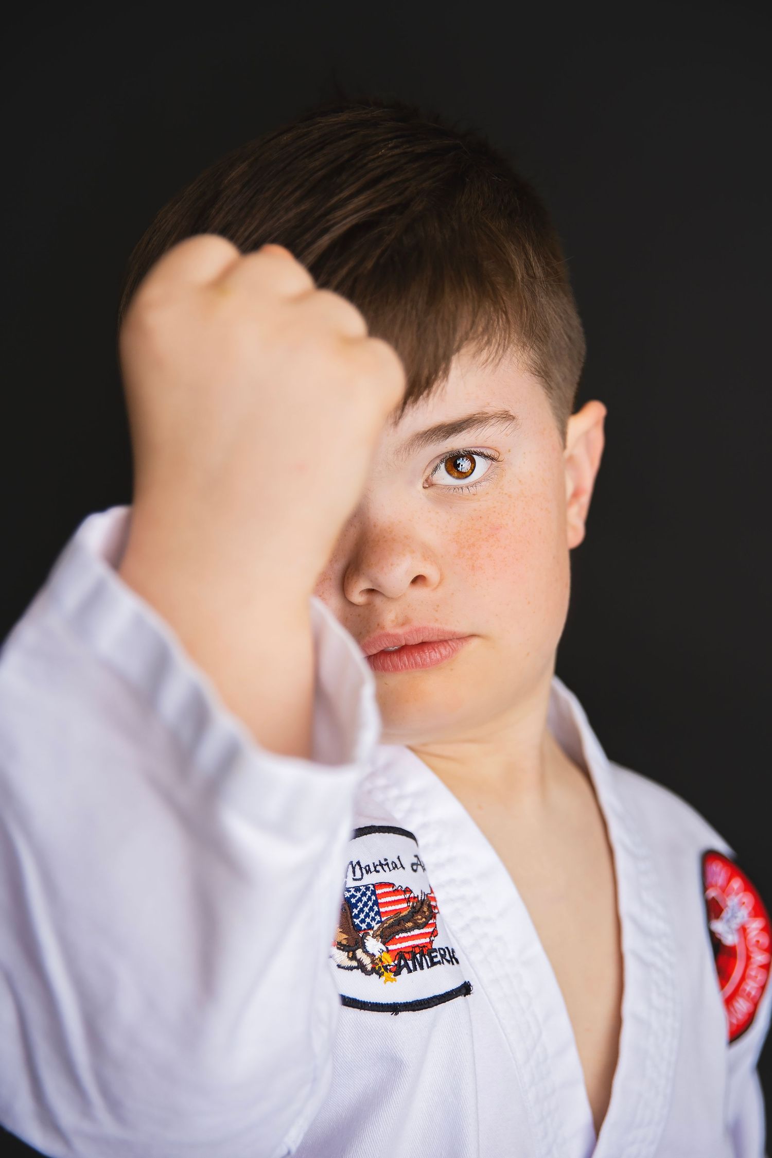 Teen martial arts student in white gi raises fist toward camera in close-up studio portrait.