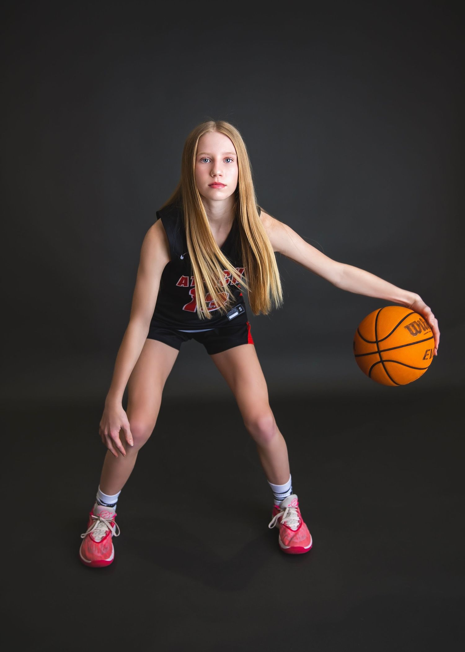 Blonde girl in Attack basketball jersey dribbling orange Wilson ball.