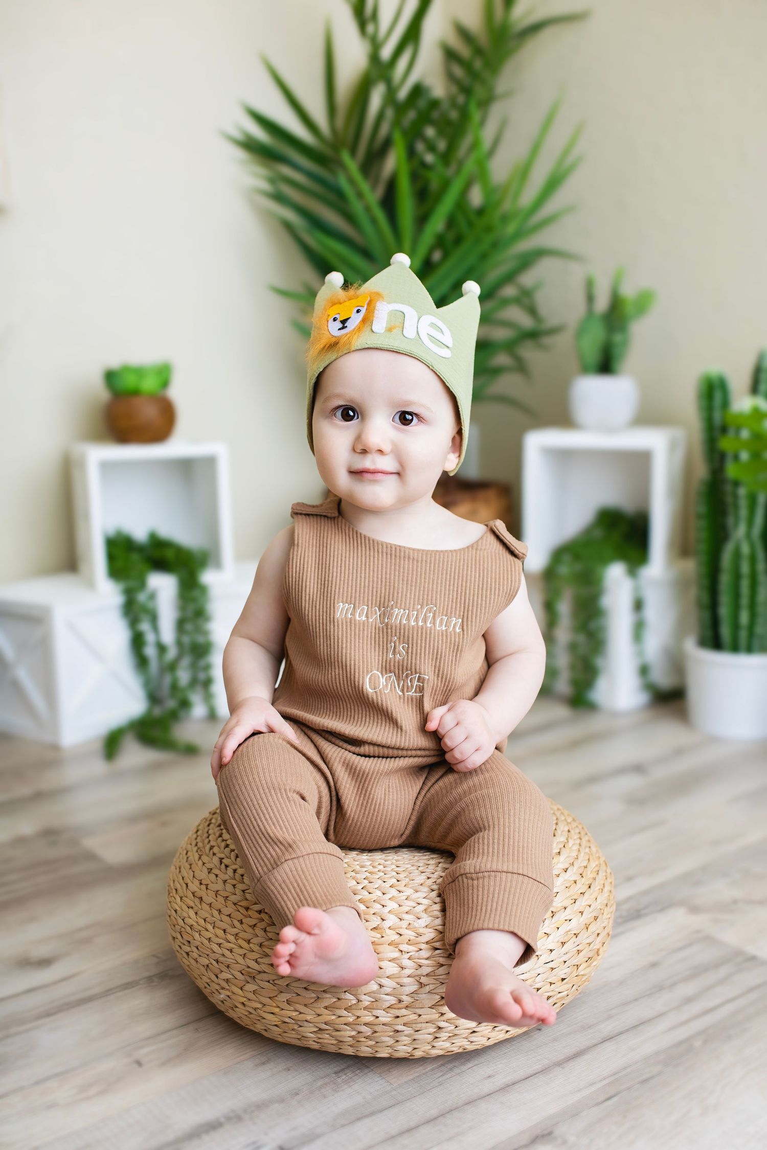 Adorable baby boy in brown outfit wearing a green lion crown celebrating his first birthday.