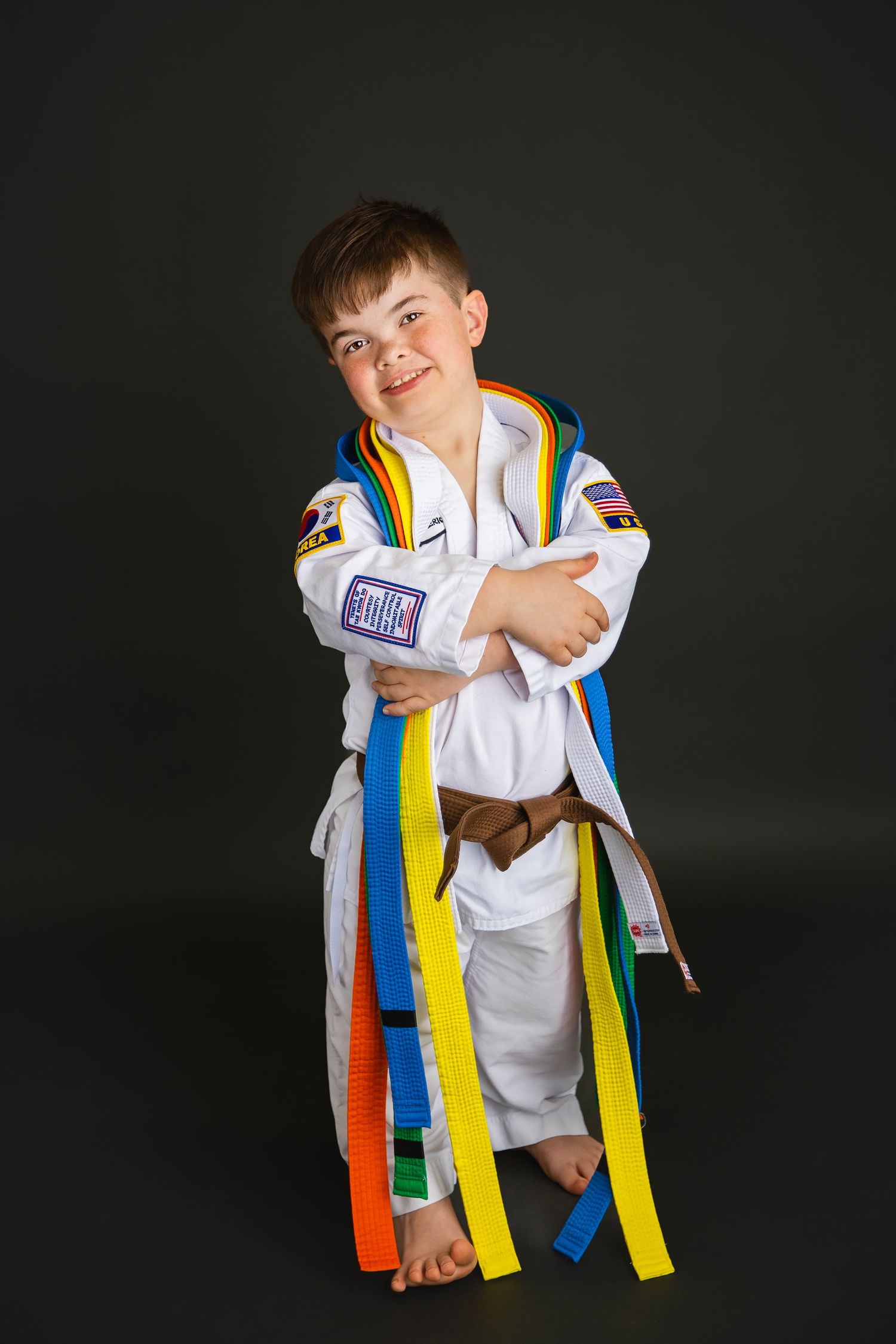 Boy in white karate gi displays collection of colorful martial arts belts in studio portrait.