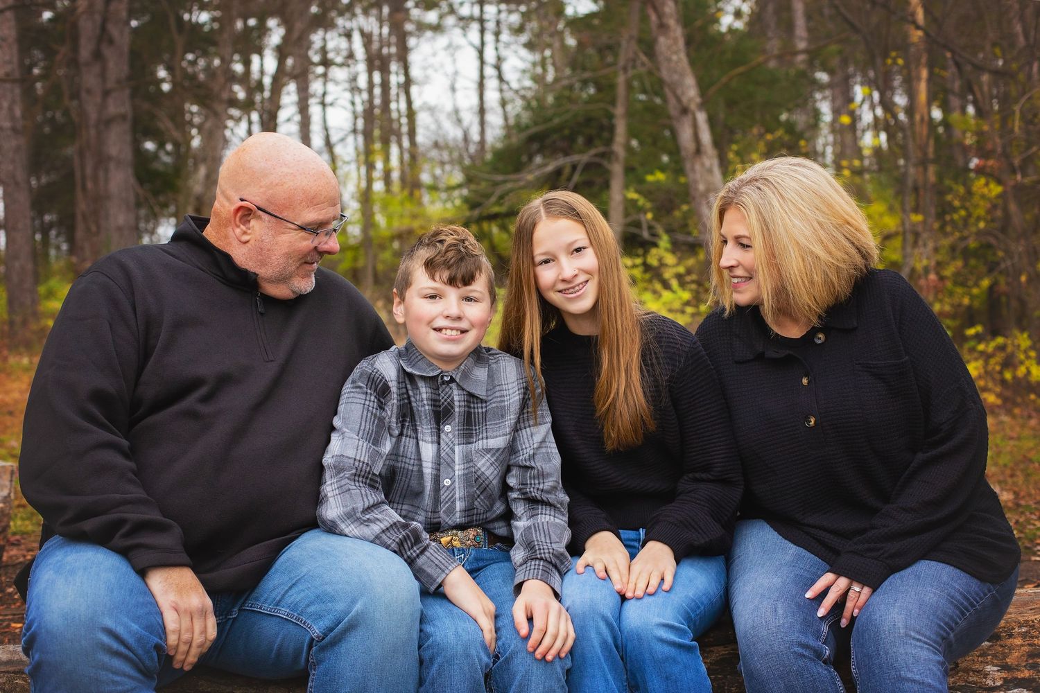 Family of four sitting together and smiling in an autumn forest.