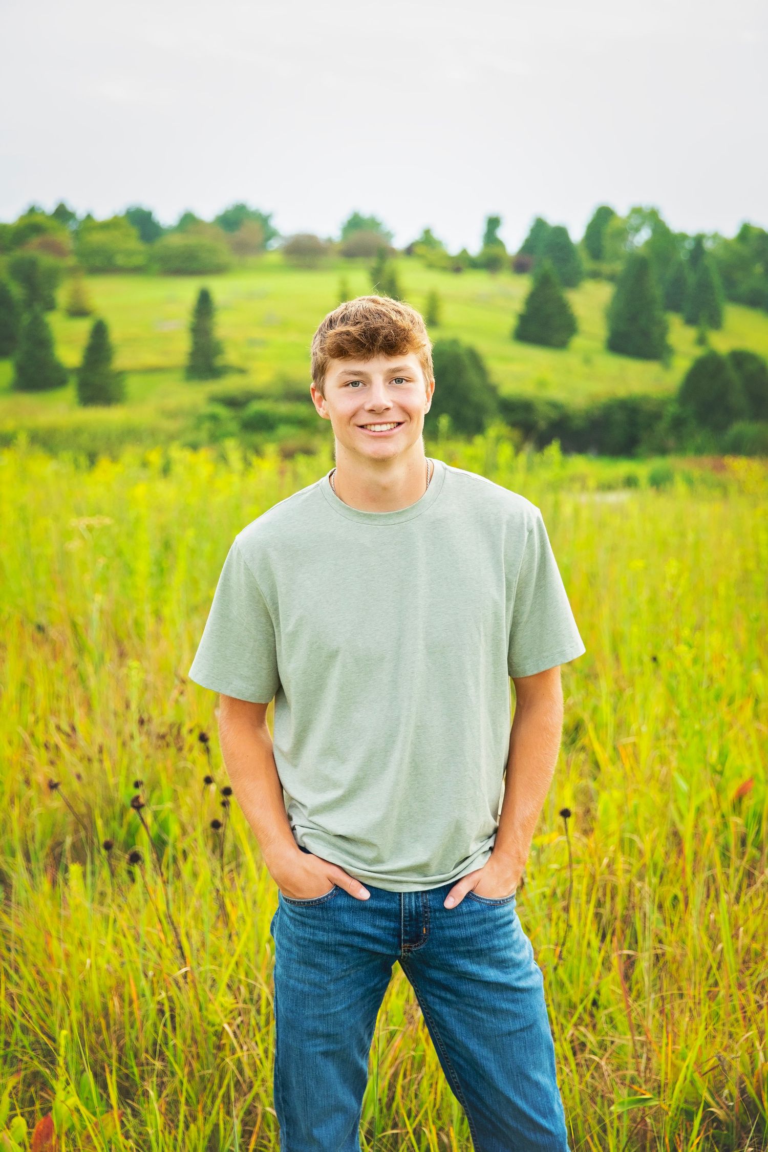 Smiling teenage boy in sage green t-shirt and jeans standing in a lush green field.