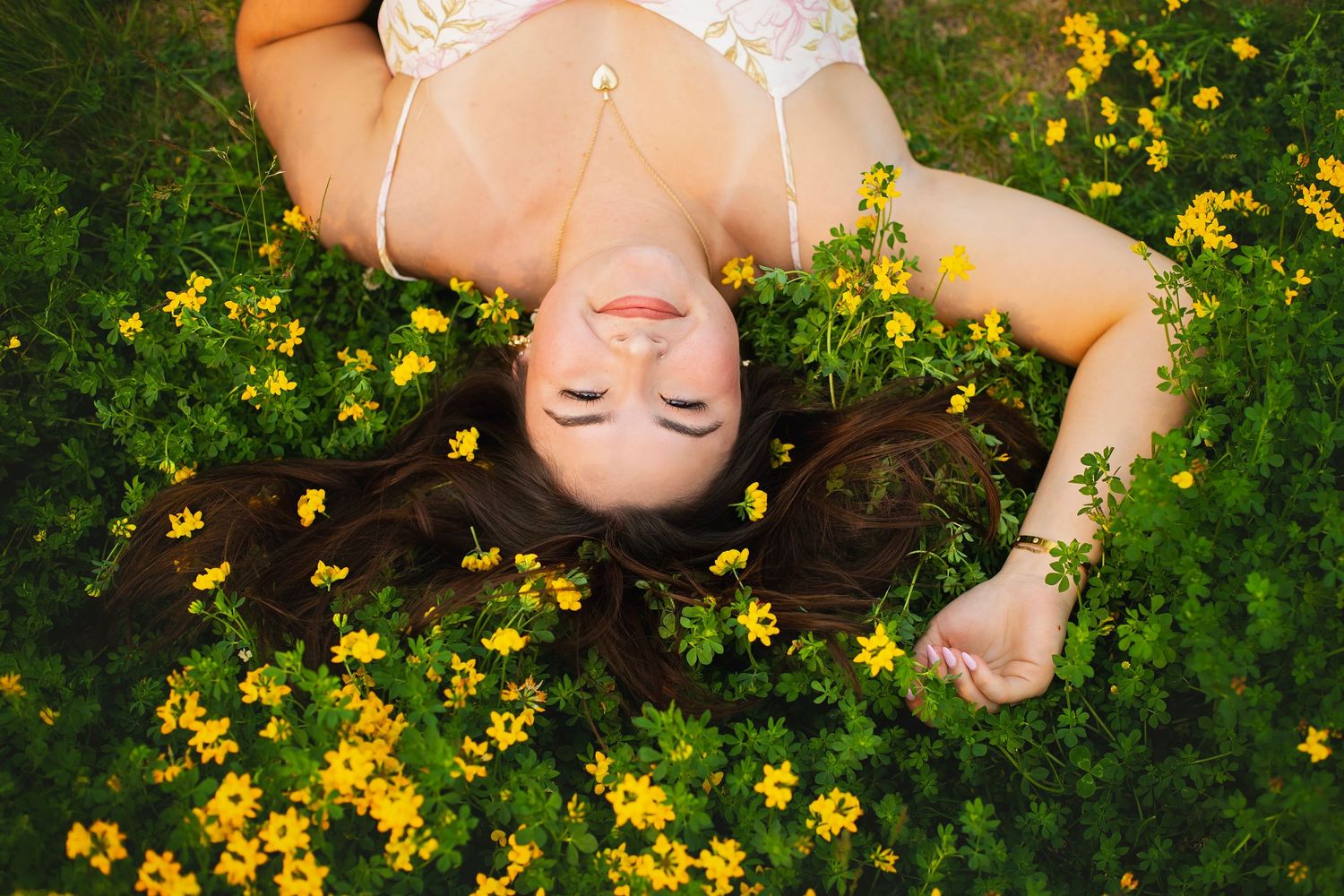 Young woman lies peacefully among bright yellow wildflowers with her hair spread out.