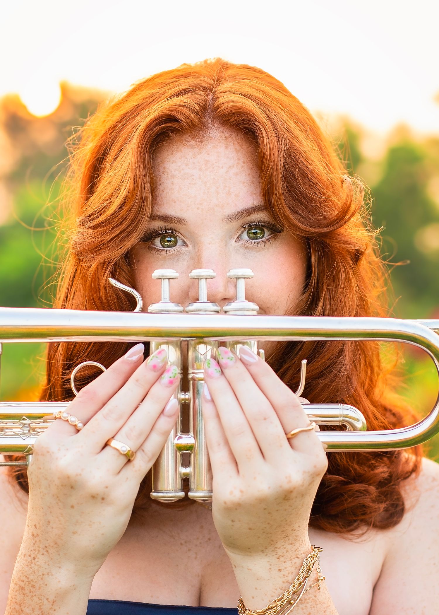 Close-up of a redhead girl with green eyes holding a silver trumpet outdoors.
