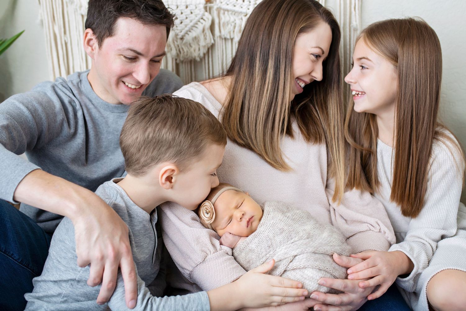 Happy family of five with parents and two children admiring their sleeping newborn baby girl.